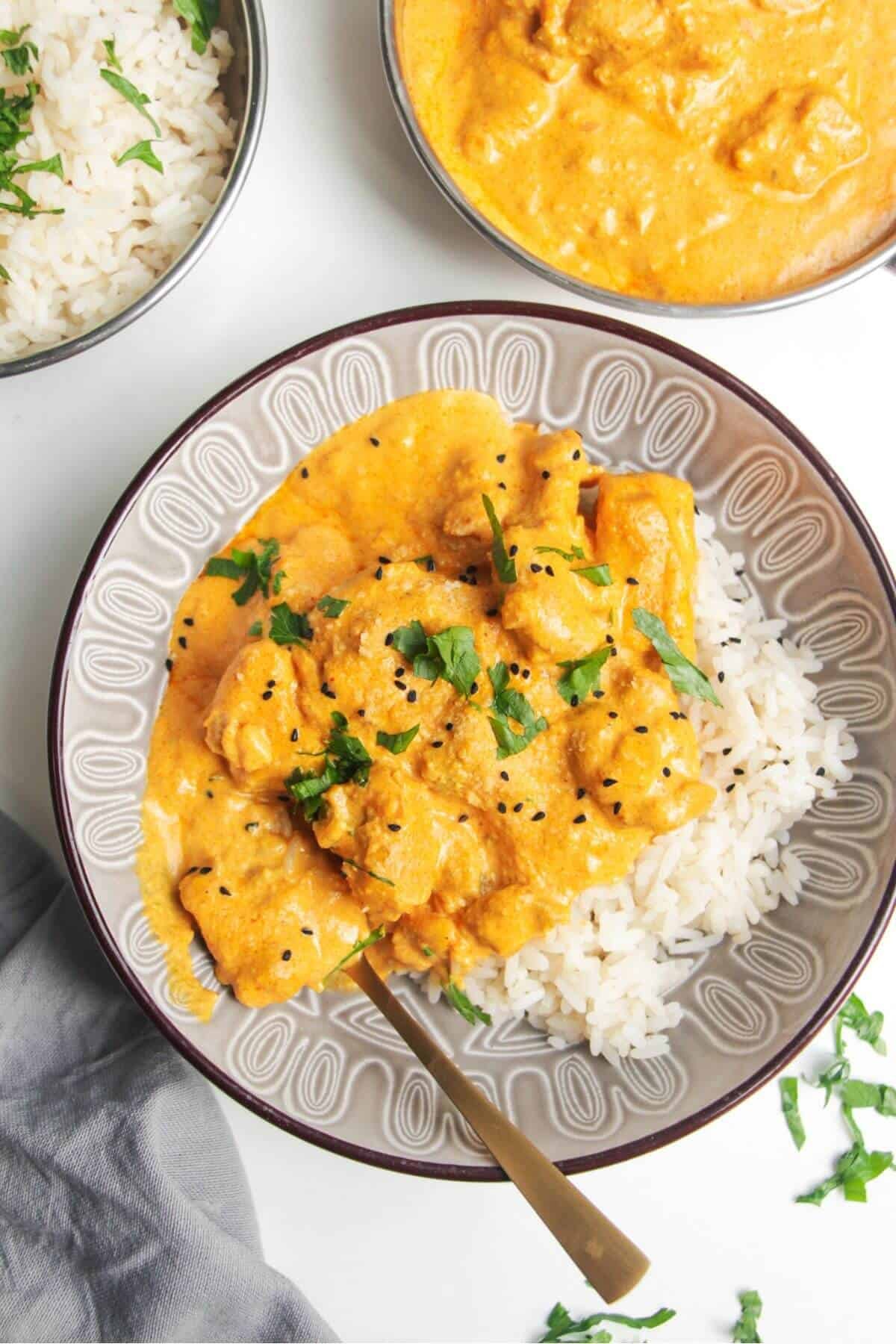 Chicken korma curry on top of rice in a bowl, with more curry and rice on the side.
