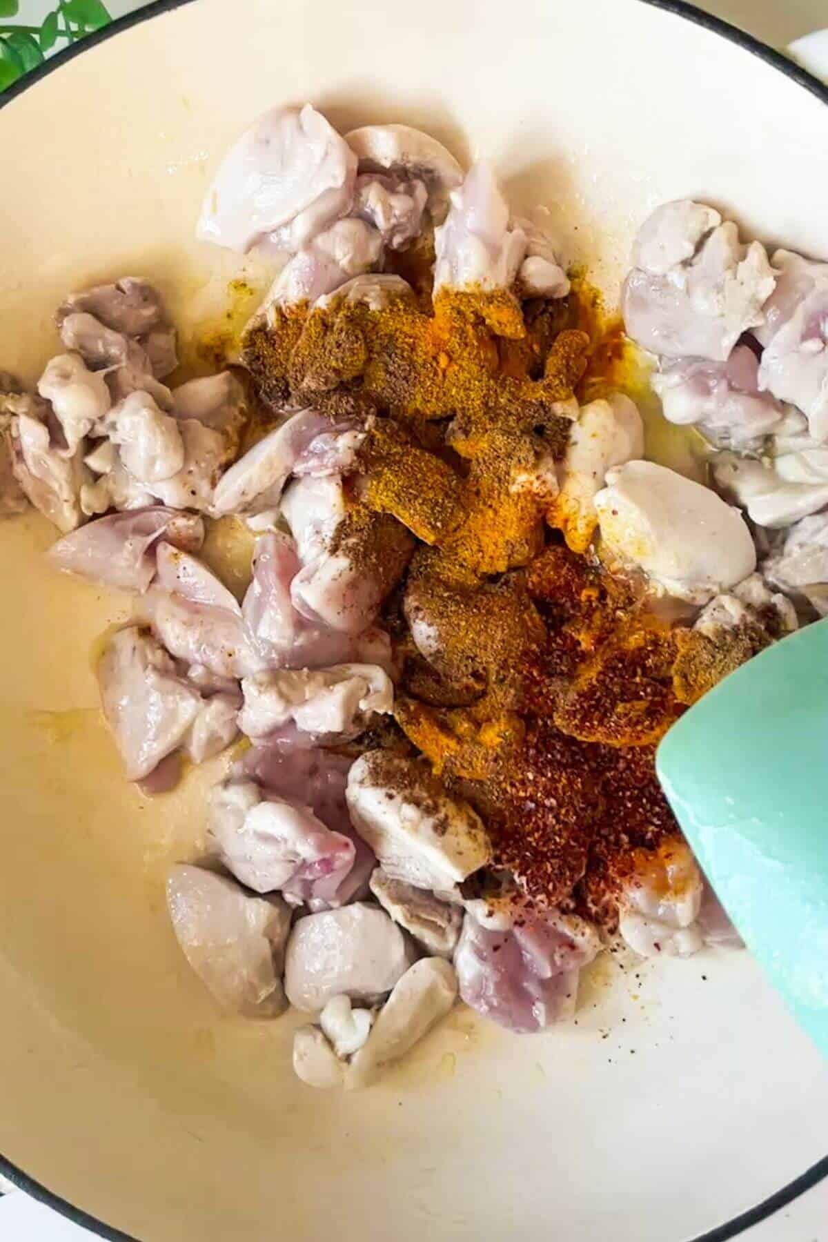 Spices added to cooked chicken pieces in a pan.