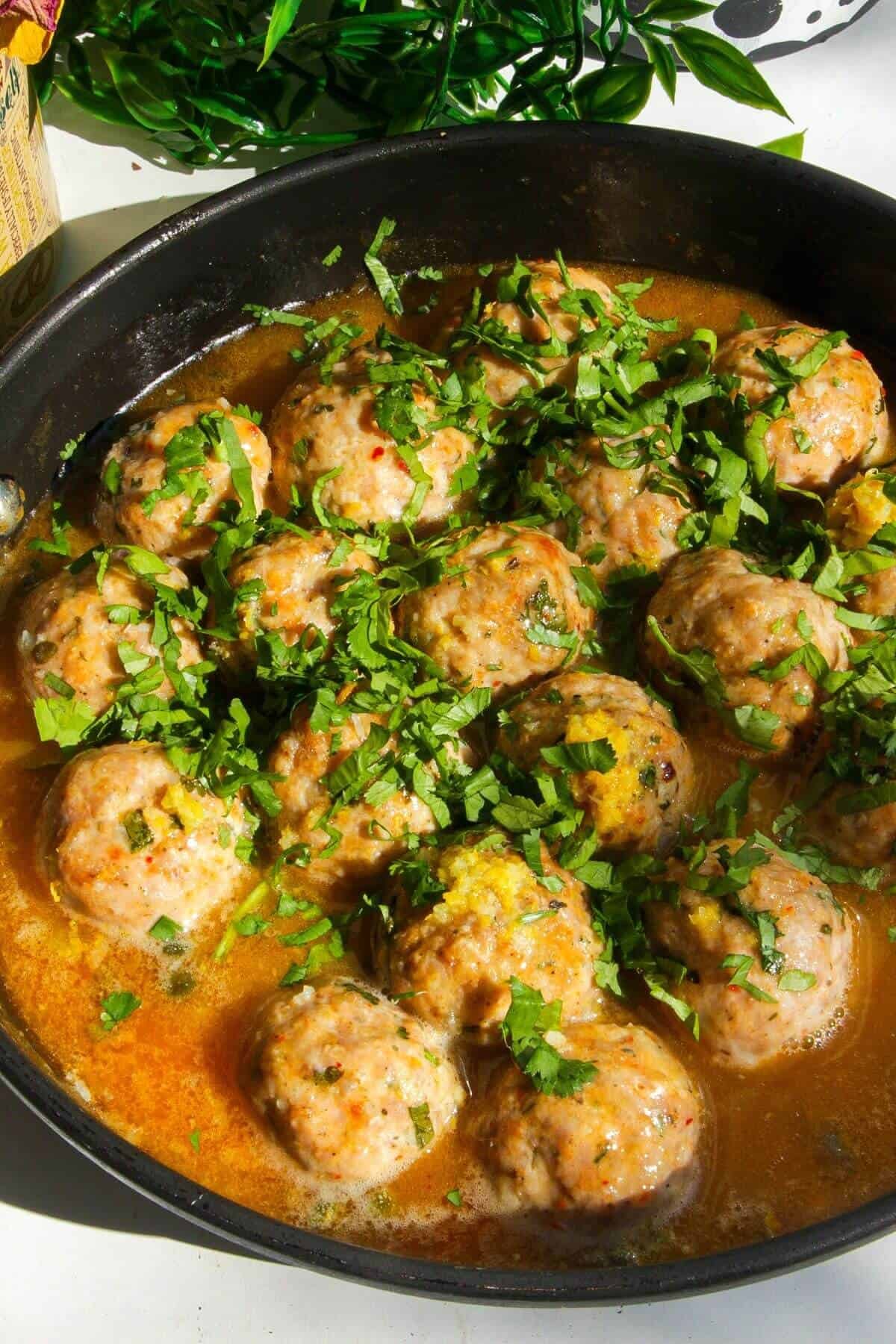 Parsley leaves scattered on top of chicken meatballs in a pan.