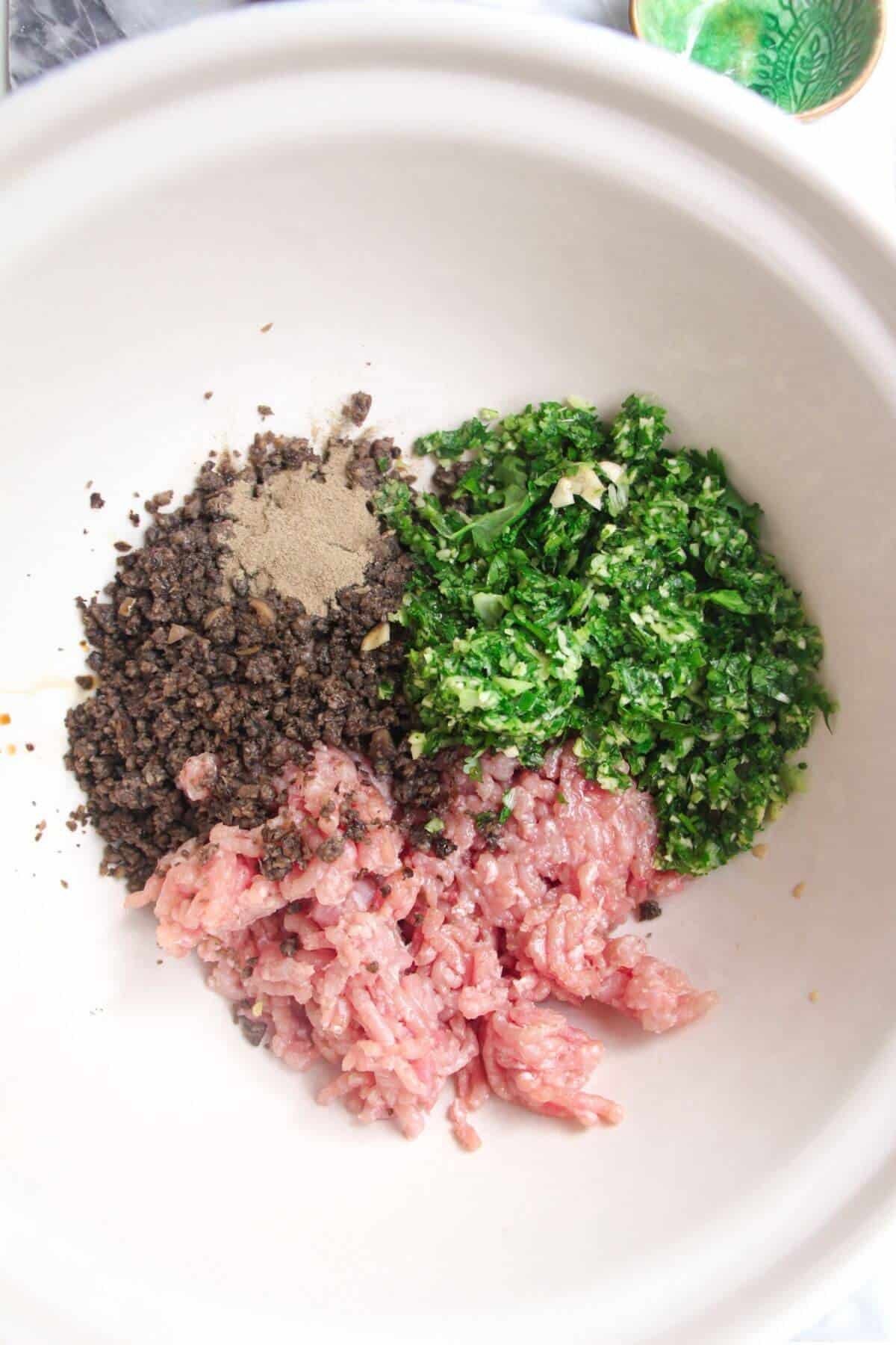 Ground chicken, herbs, mushrooms and seasoning in a large white mixing bowl.