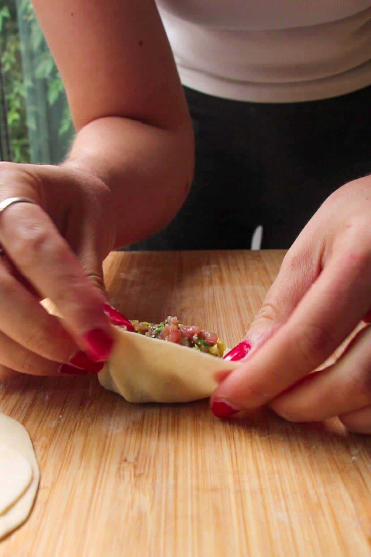 Hands folding dumpling on a wooden board.