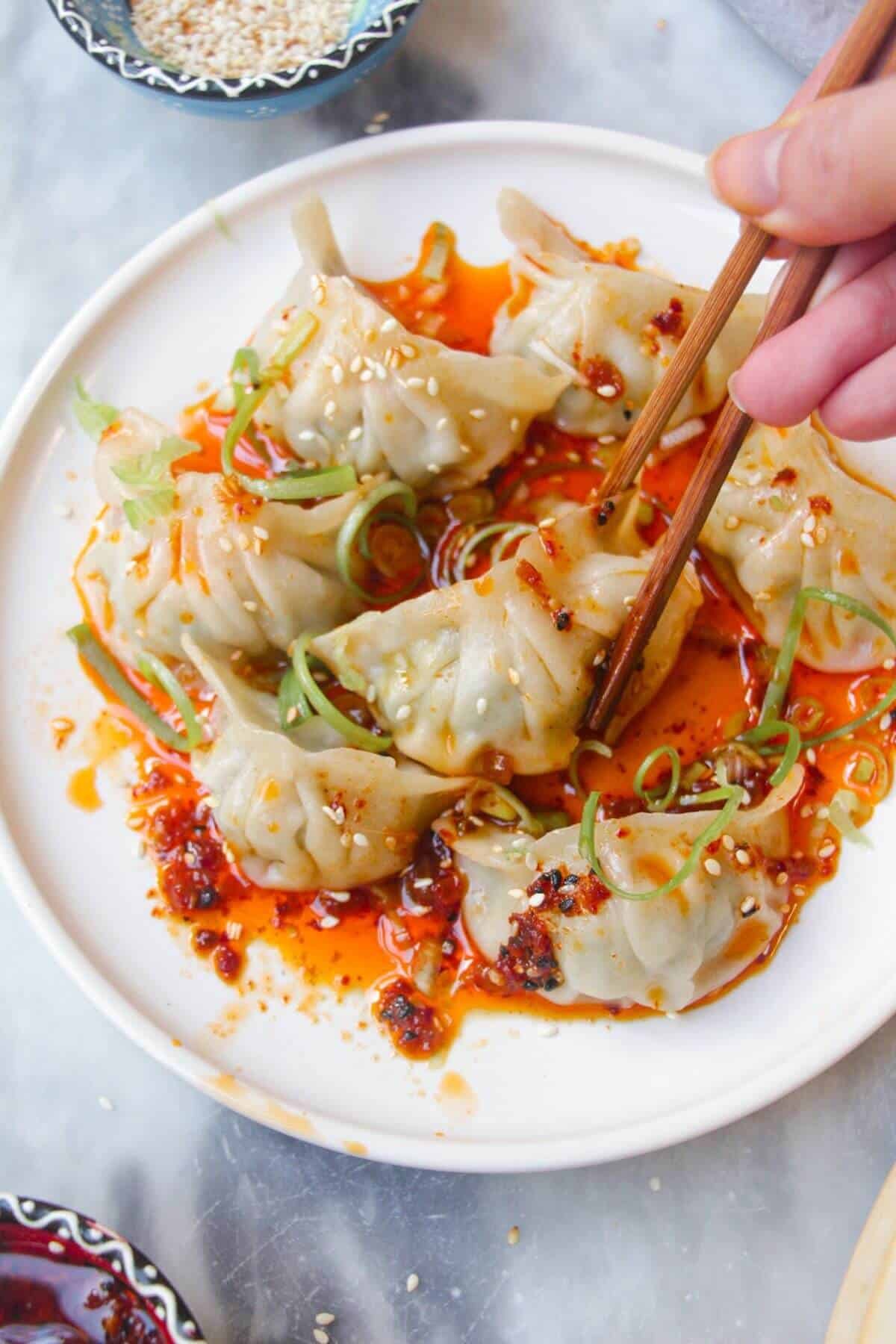 Steamed dumplings on a small white plate, drizzled with chilli oil.