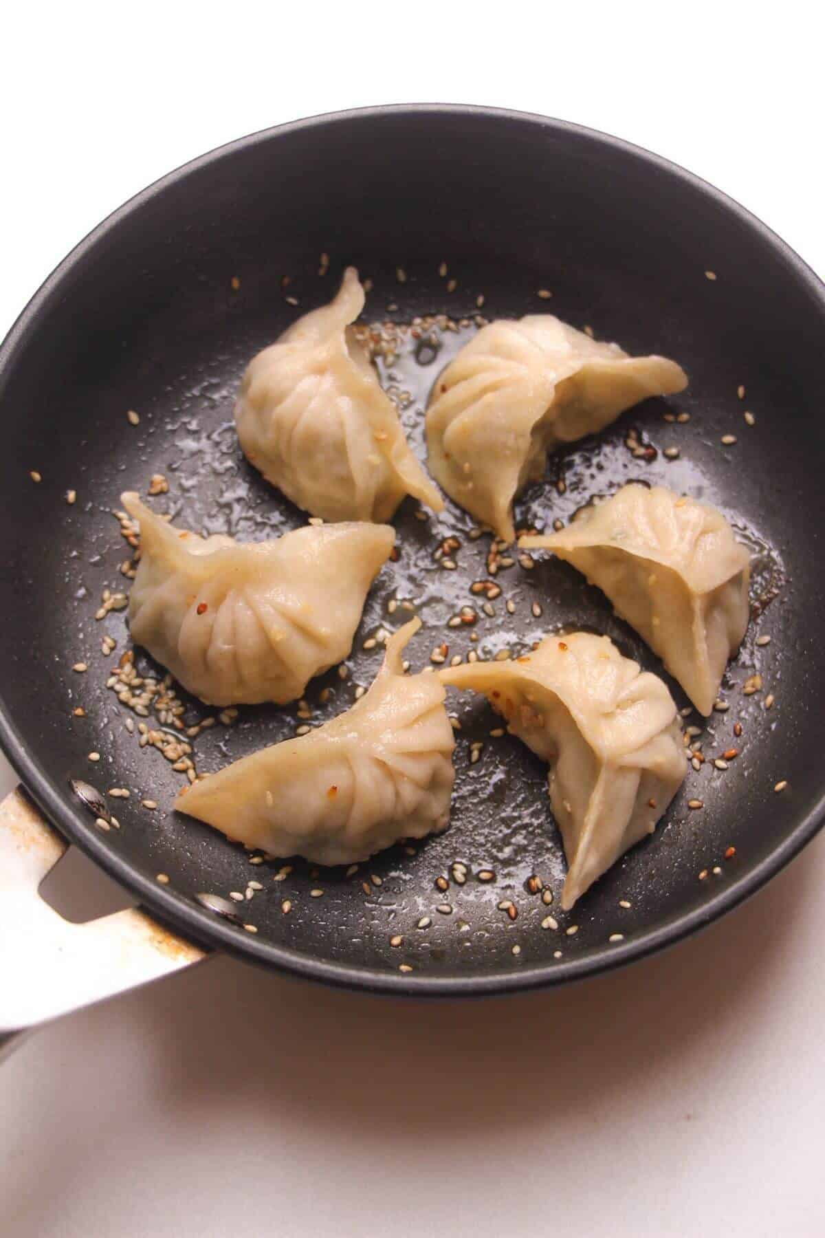 Six pan fried dumplings in a small pan.