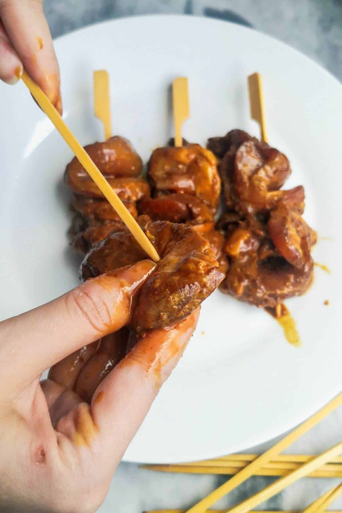 Hand threading marinated chicken onto skewers.