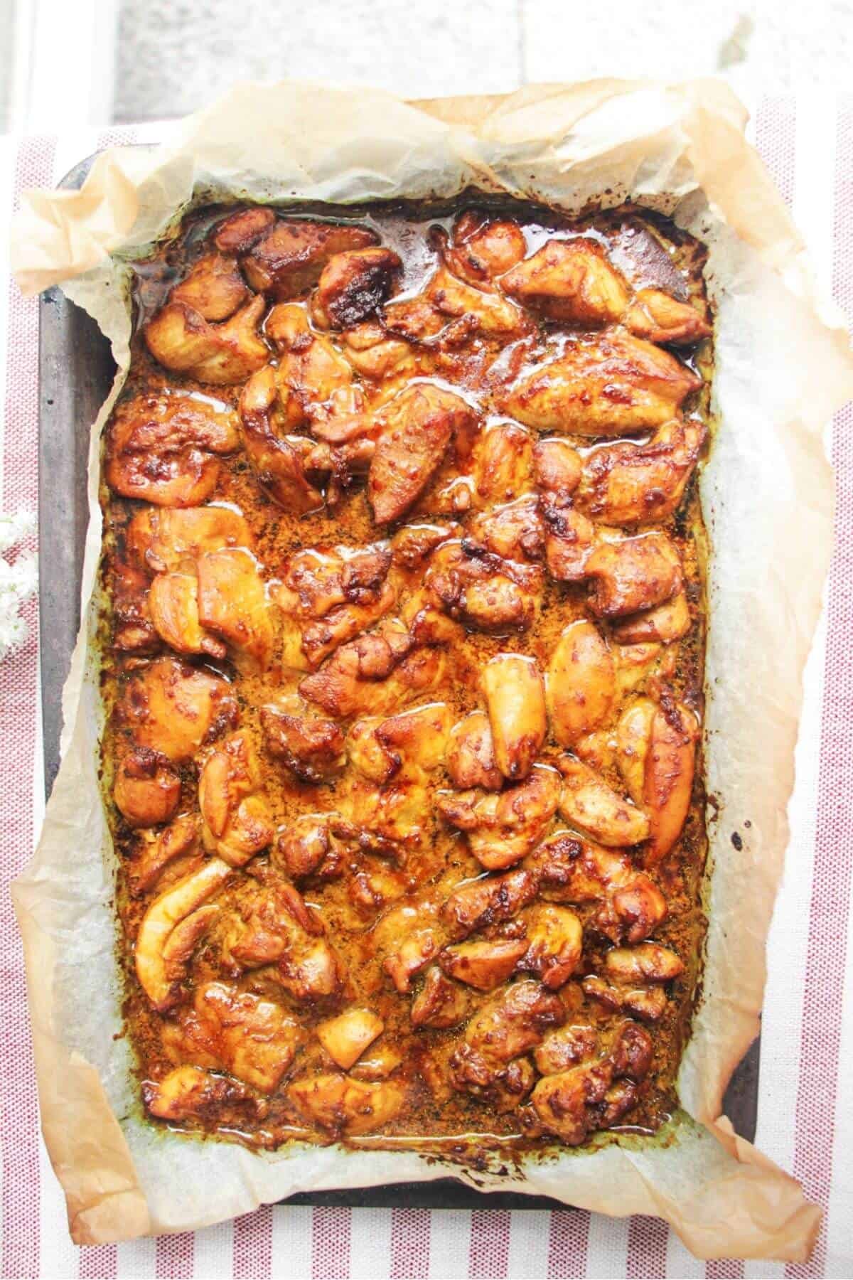 Charred chicken pieces in a lined oven tray.