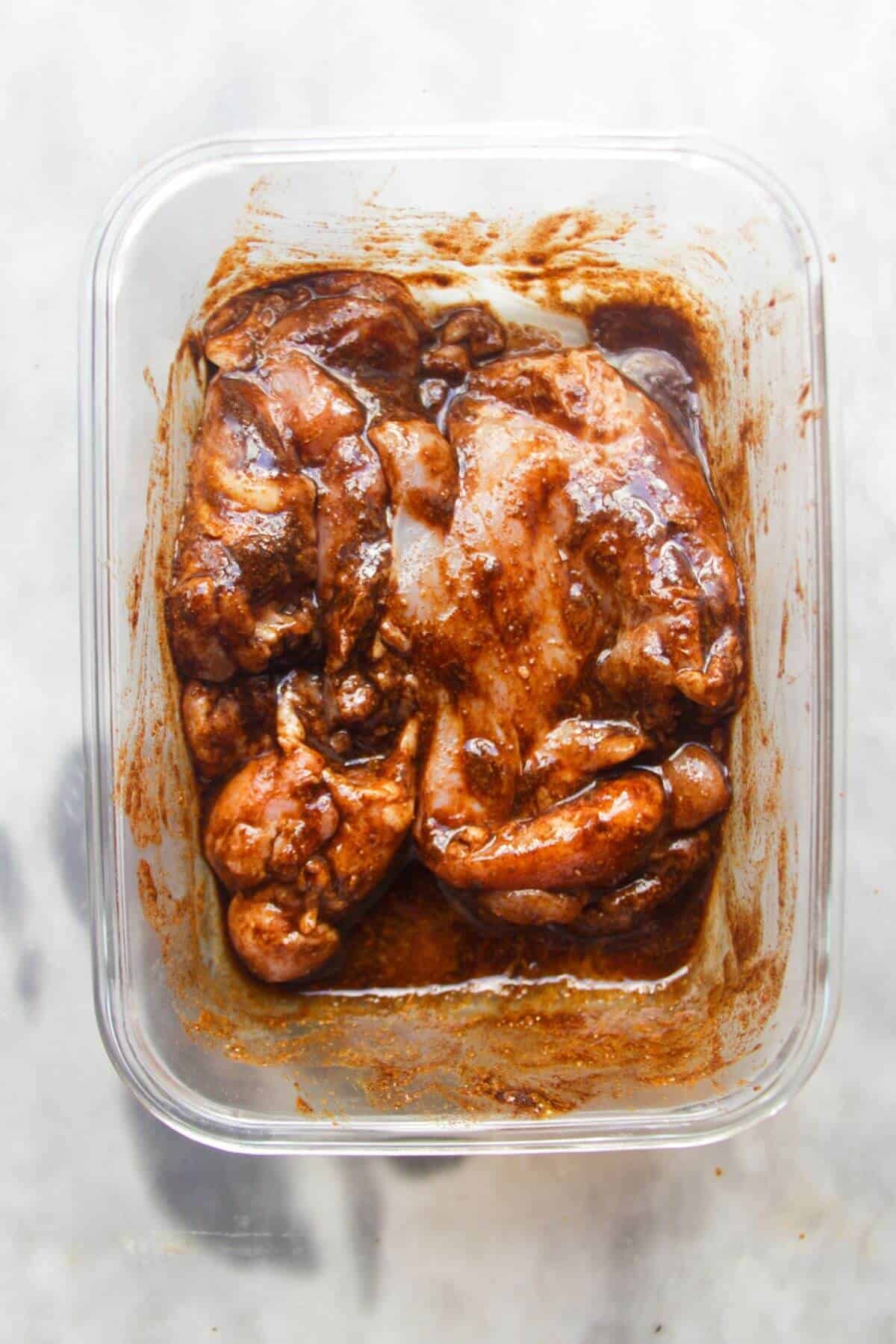Chicken thighs marinating in shawarma spices in a small glass container.
