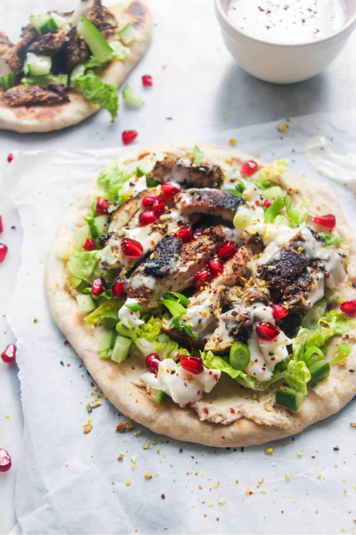 Chicken shawarma wrap on a grey marble background with a small bowl of tahini sauce on the side.