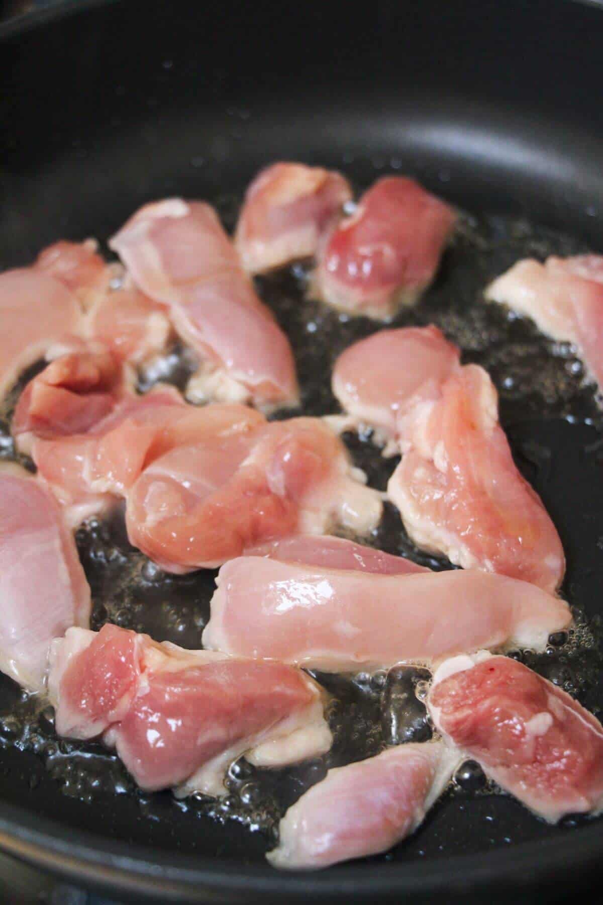 Chicken strips cooking in a large frying pan.