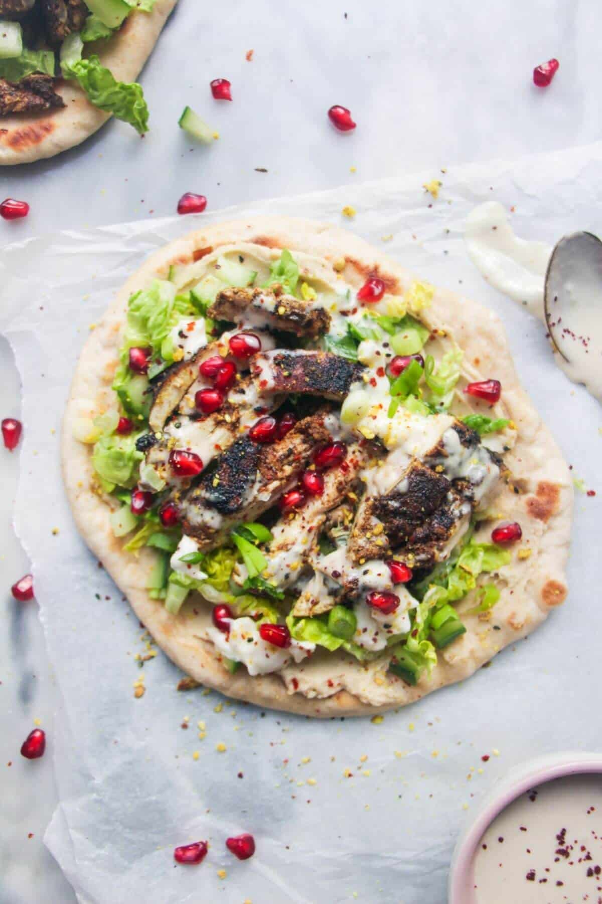 Chicken shawarma wrap on a grey marble background with a small bowl of tahini sauce on the side.