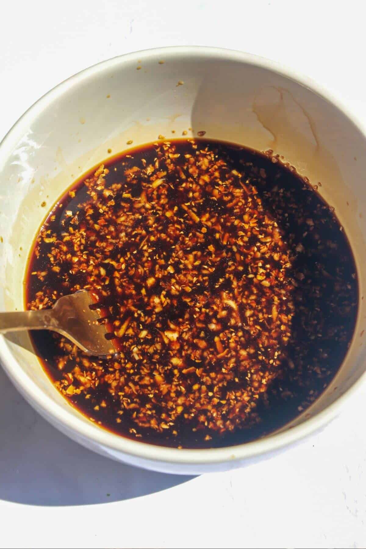 Fork mixing teriyaki sauce in a small white bowl.