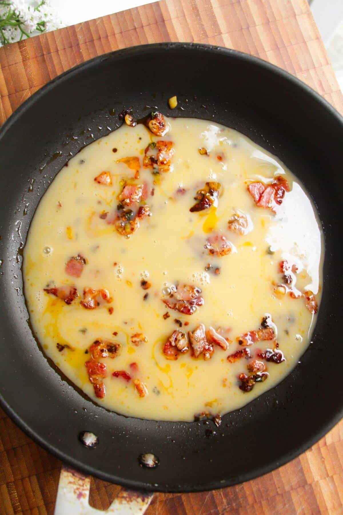 Eggs in a pan with bacon and scallions.