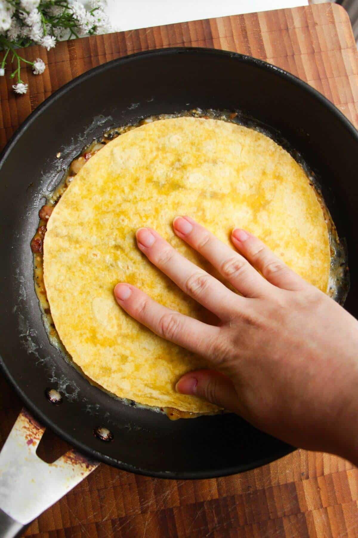 Tortilla wrap pressed on eggs and bacon in a pan.