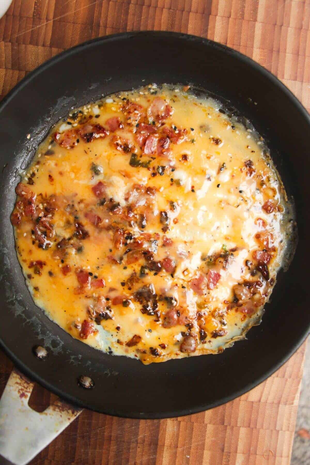 Eggs setting in a pan with bacon and scallions.