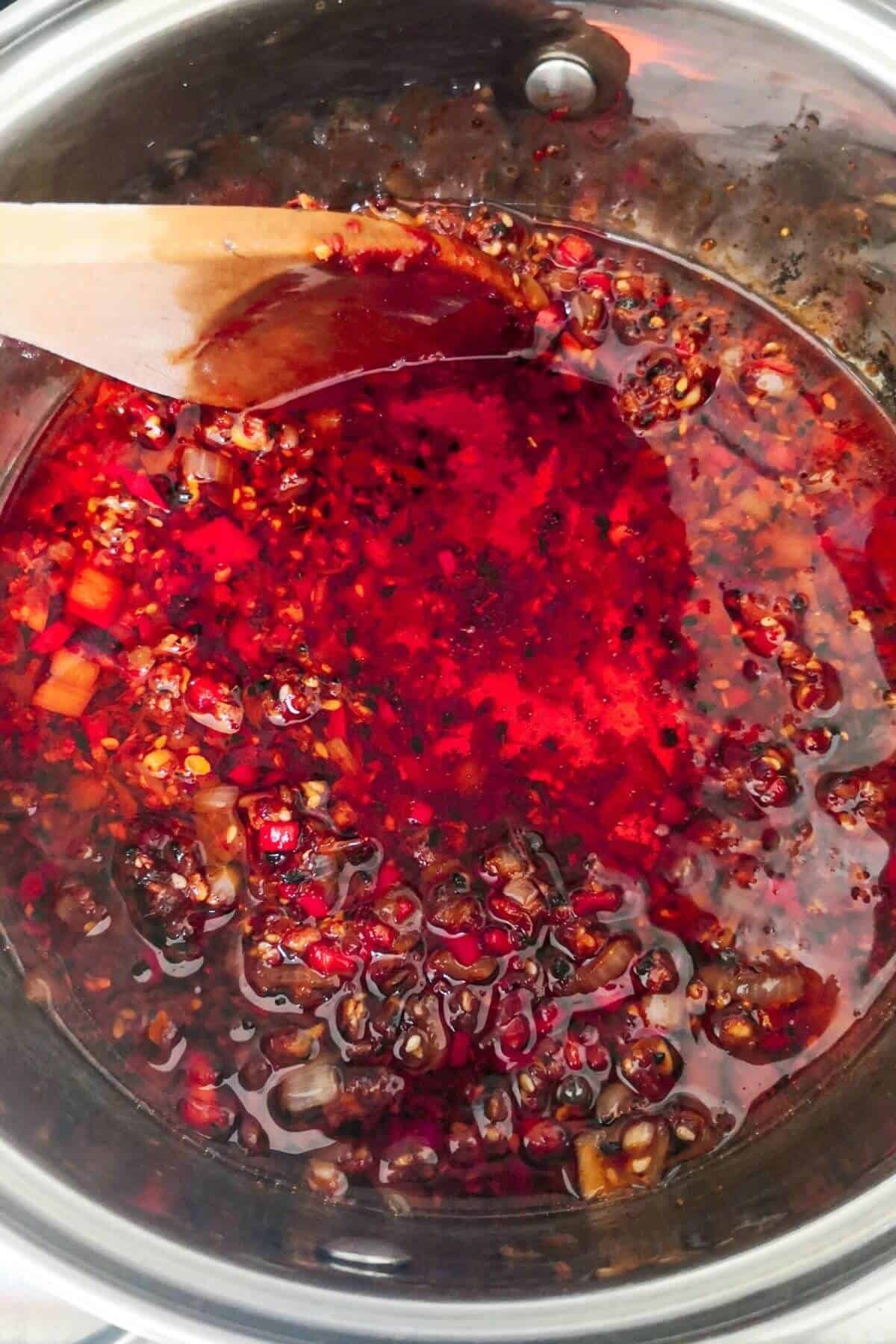 Chilli oil cooking in a small silver pot with a wooden spoon inside.