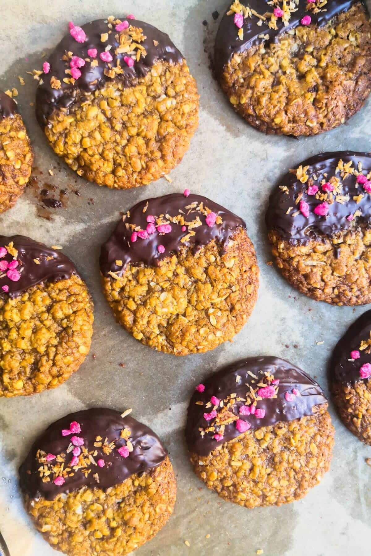 Chocolate dipped Anzac biscuits topped with rose and coconut on a lined tray.