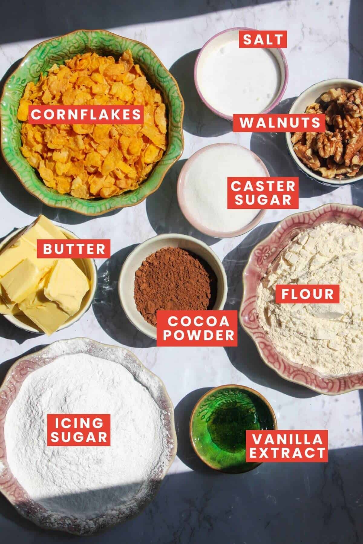 Ingredients for chocolate Afghan biscuits laid out on a white marble background and labelled.
