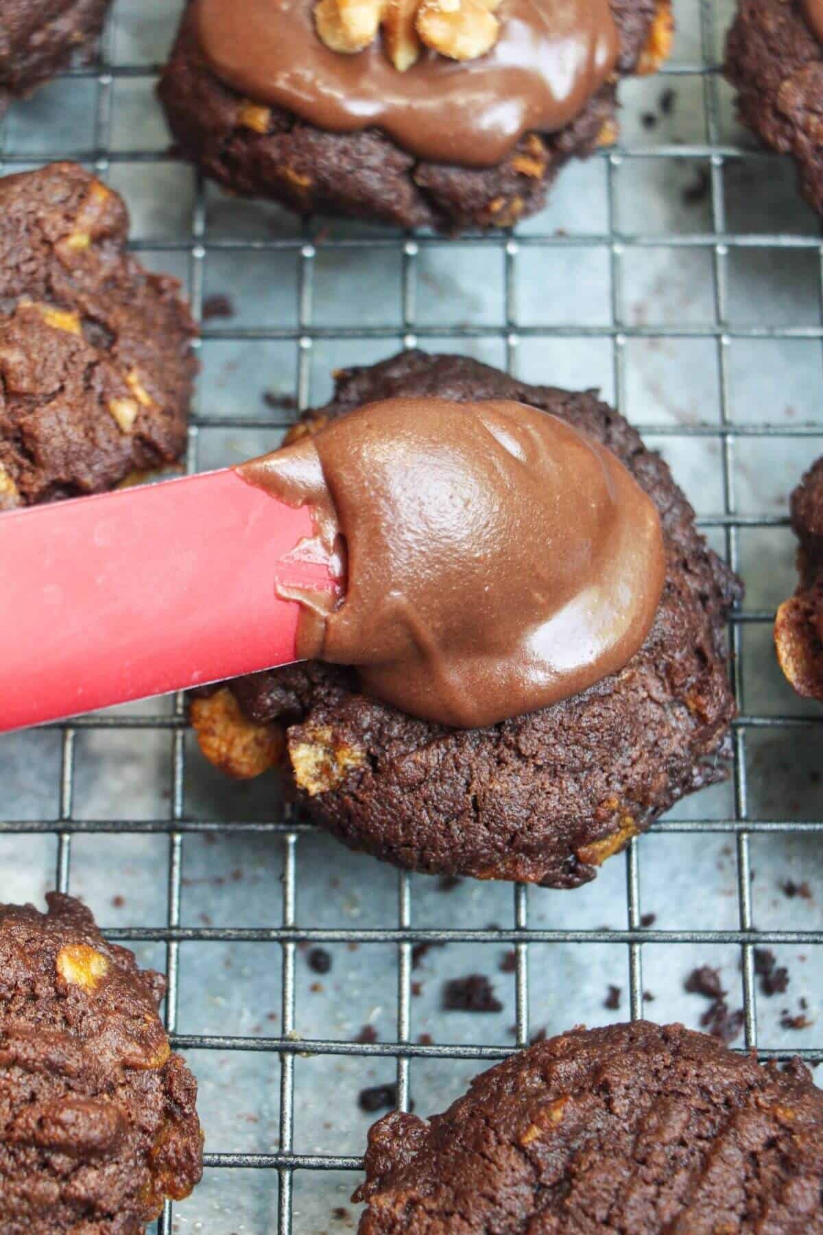 Red spatula spreading chocolate icing on top of chocolate Afghan biscuits.