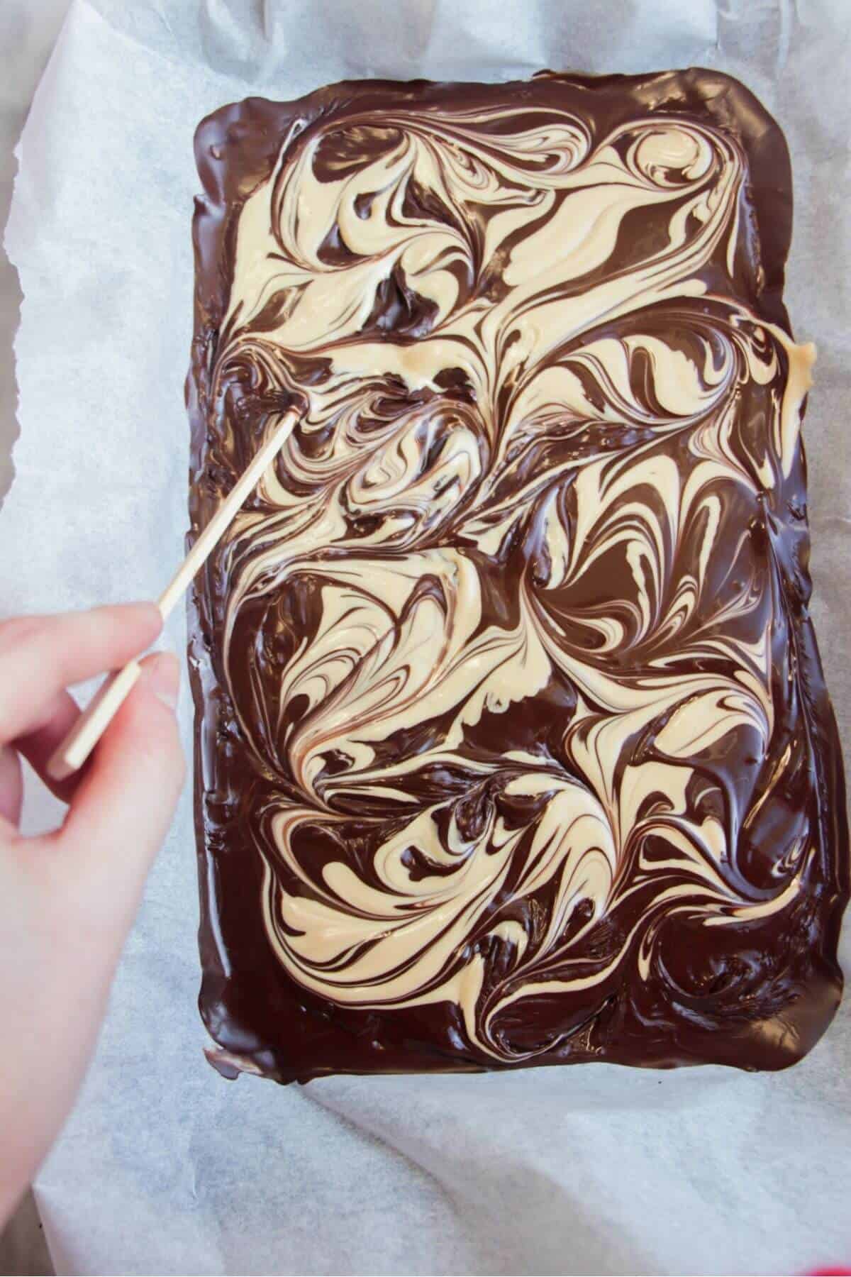 Hand holding a skewer, marbling melted white chocolate through melted dark chocolate.