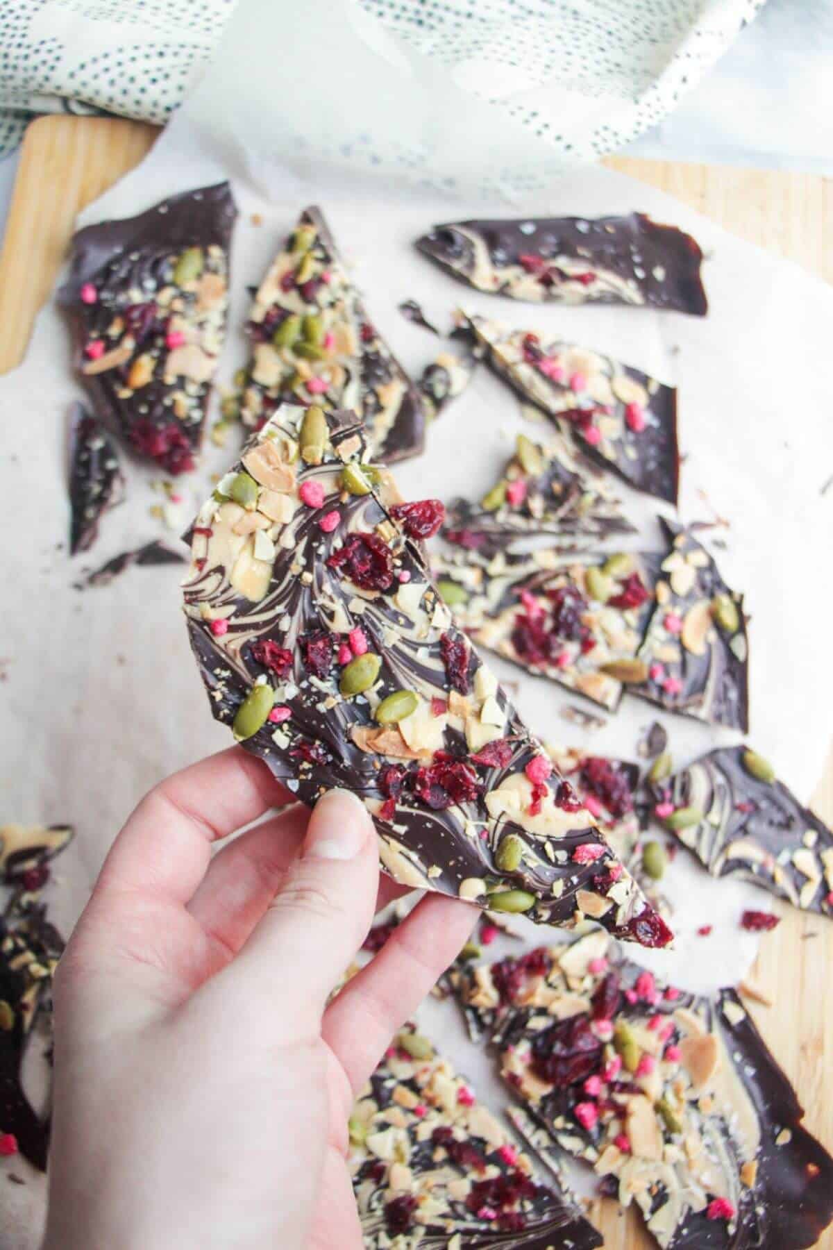 Hand holding up a piece of chocolate almond bark with more chocolate bark in the background.