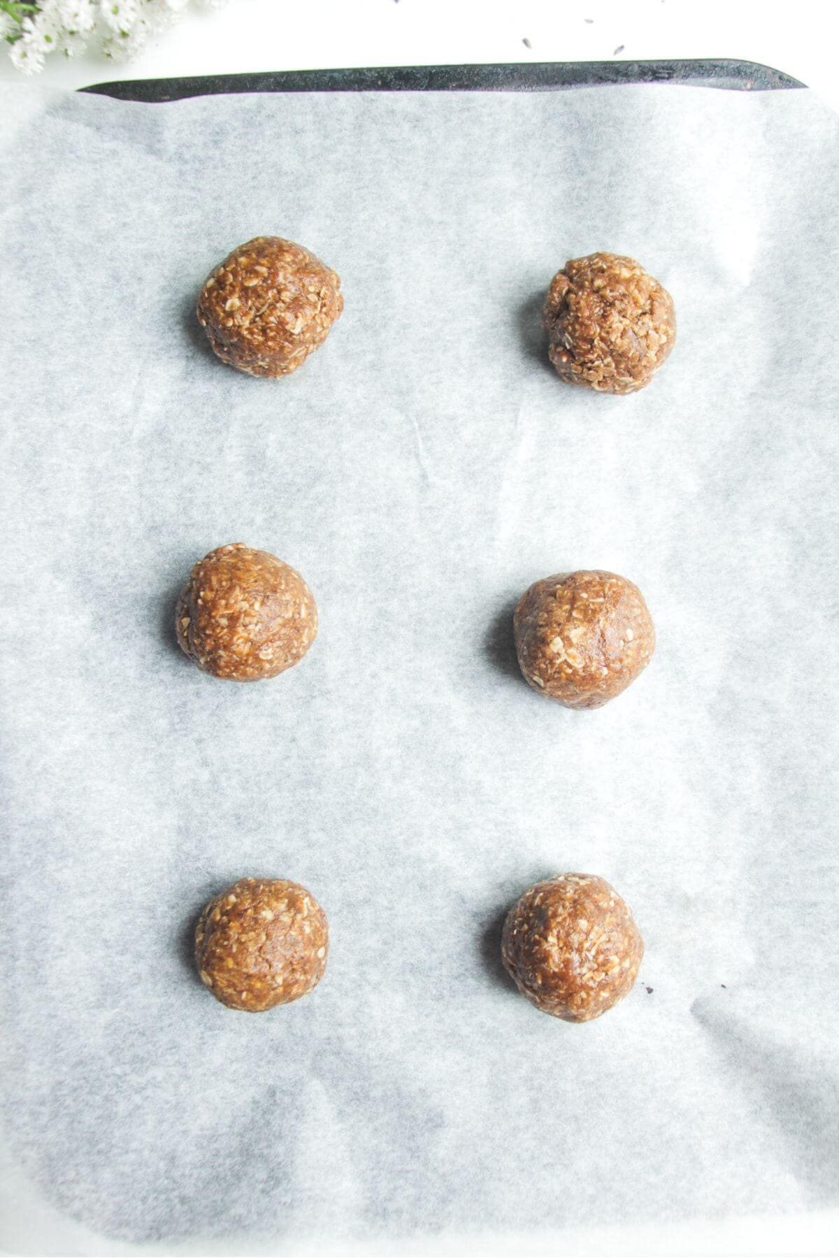 Six Anzac bisciut dough balls on a lined oven tray.