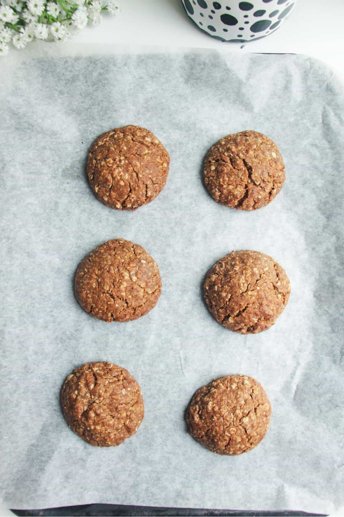 Baked Anzac bisciuts on a lined oven tray.