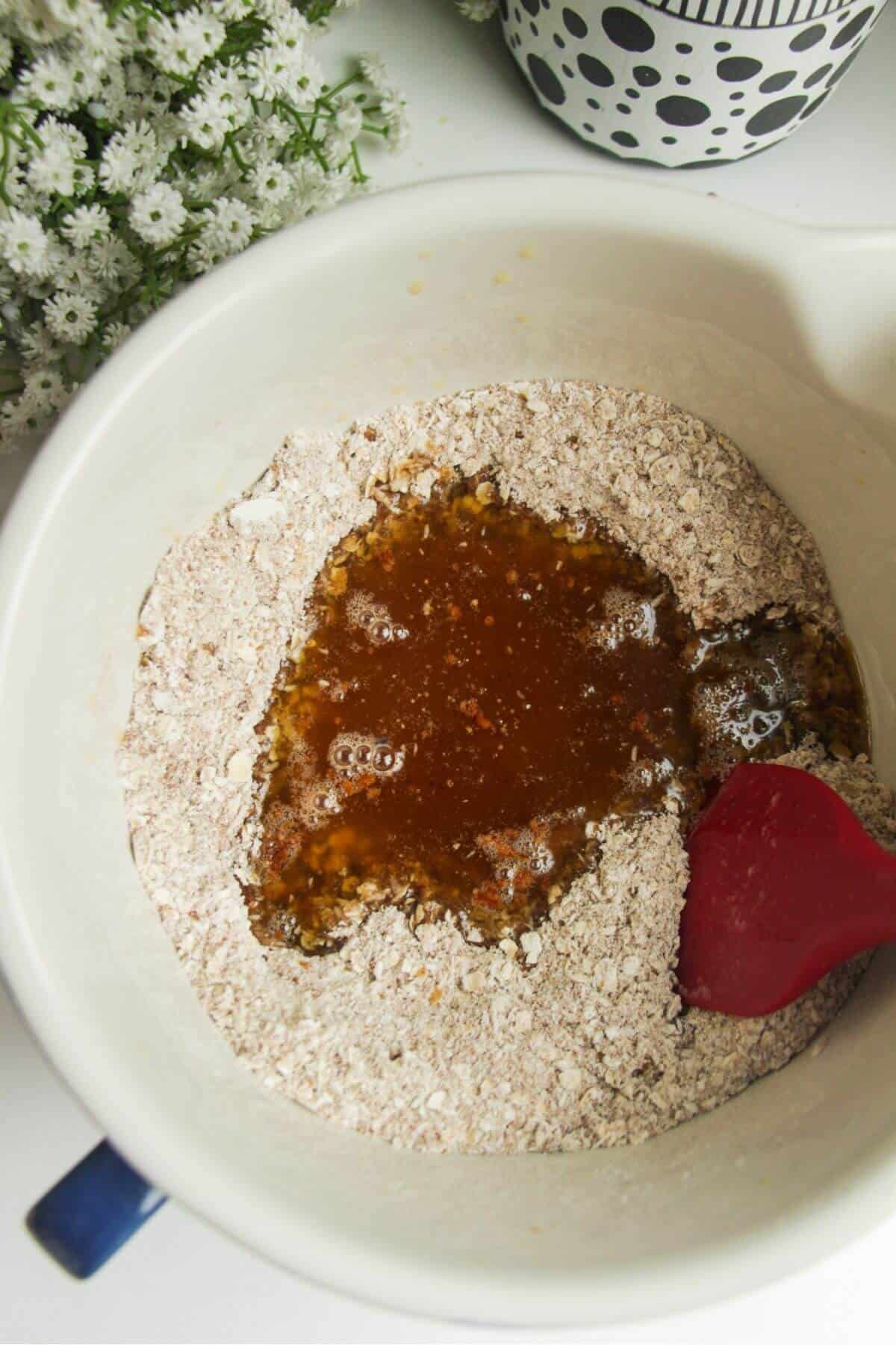 Brown butter and golden syrup added to dry ingredients in a mixing bowl.