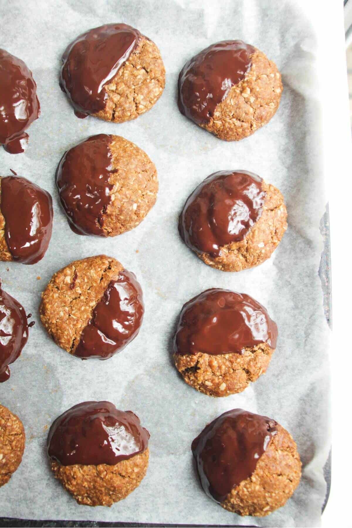 Anzac biscuits dunked in dark chocolate on an oven tray.