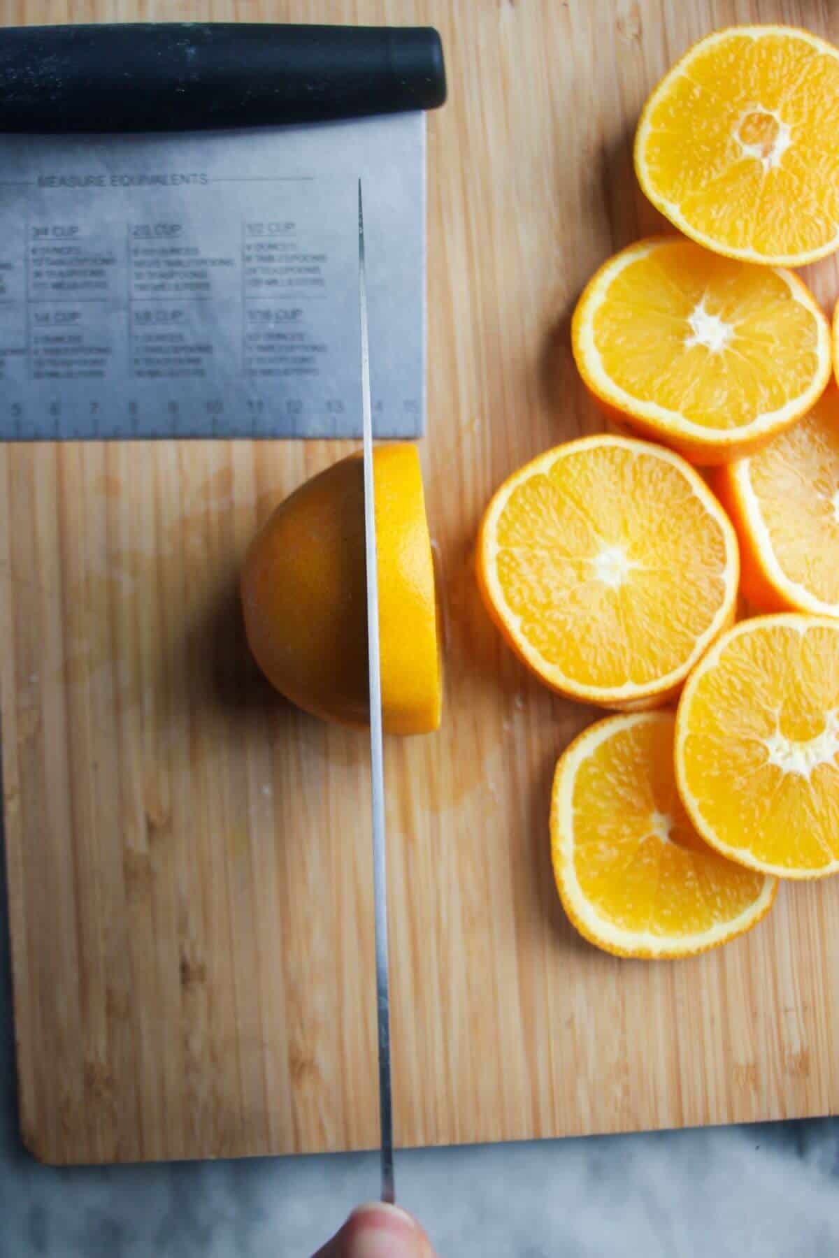 A knife cutting an orange into thick slices.