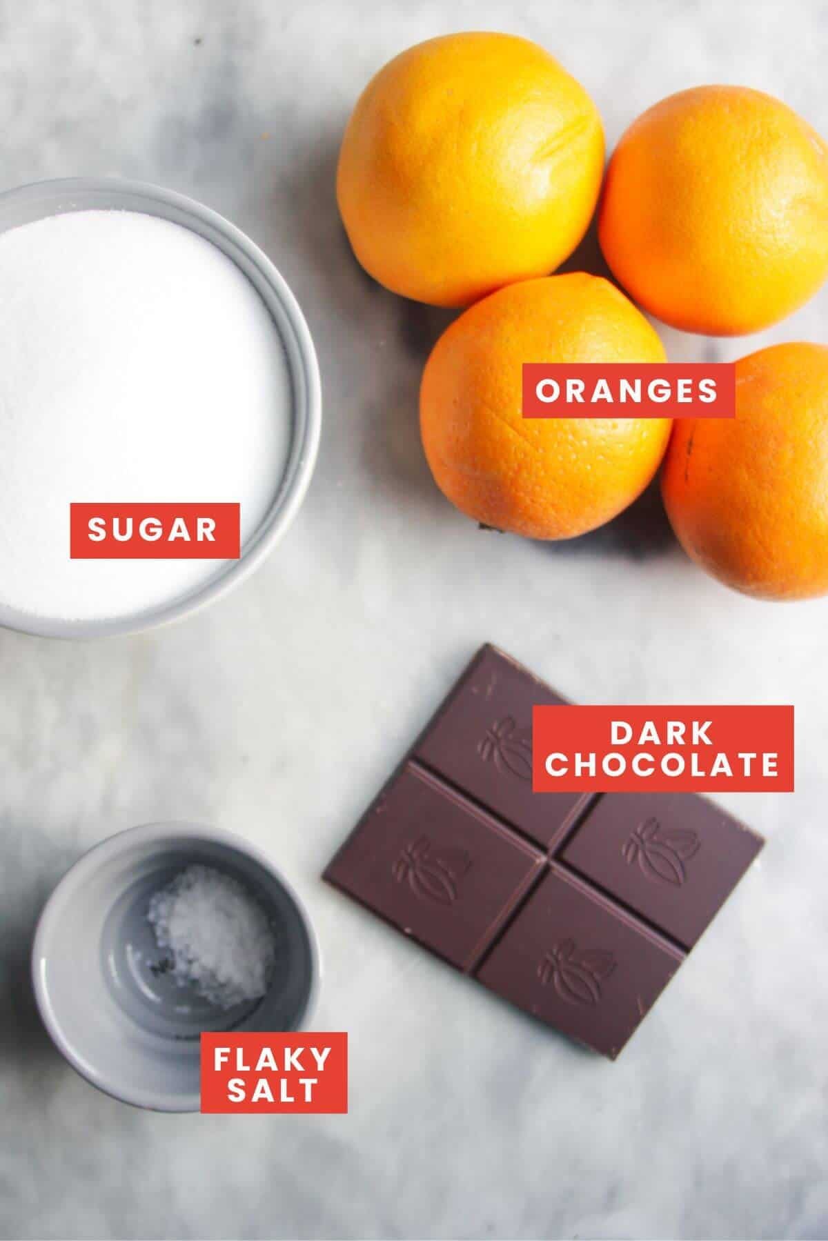 Ingredients for candied orange slices laid out on a grey marble background and labelled.
