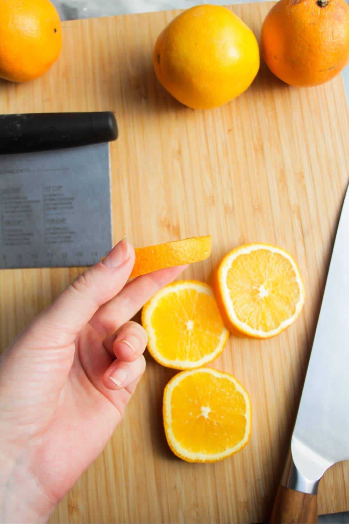 Hand holding up a sliced orange with more orange slices in the background.