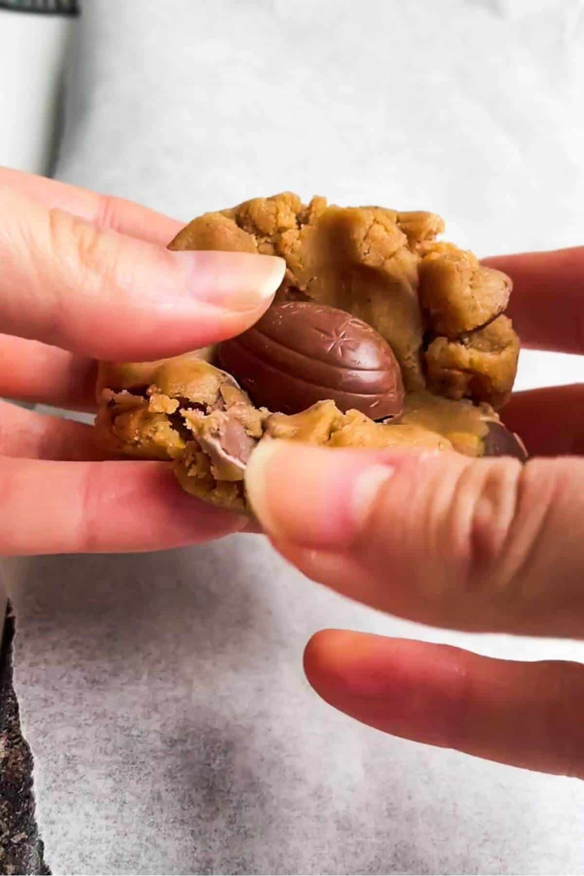 Hands folding mini creme egg into cookie dough.