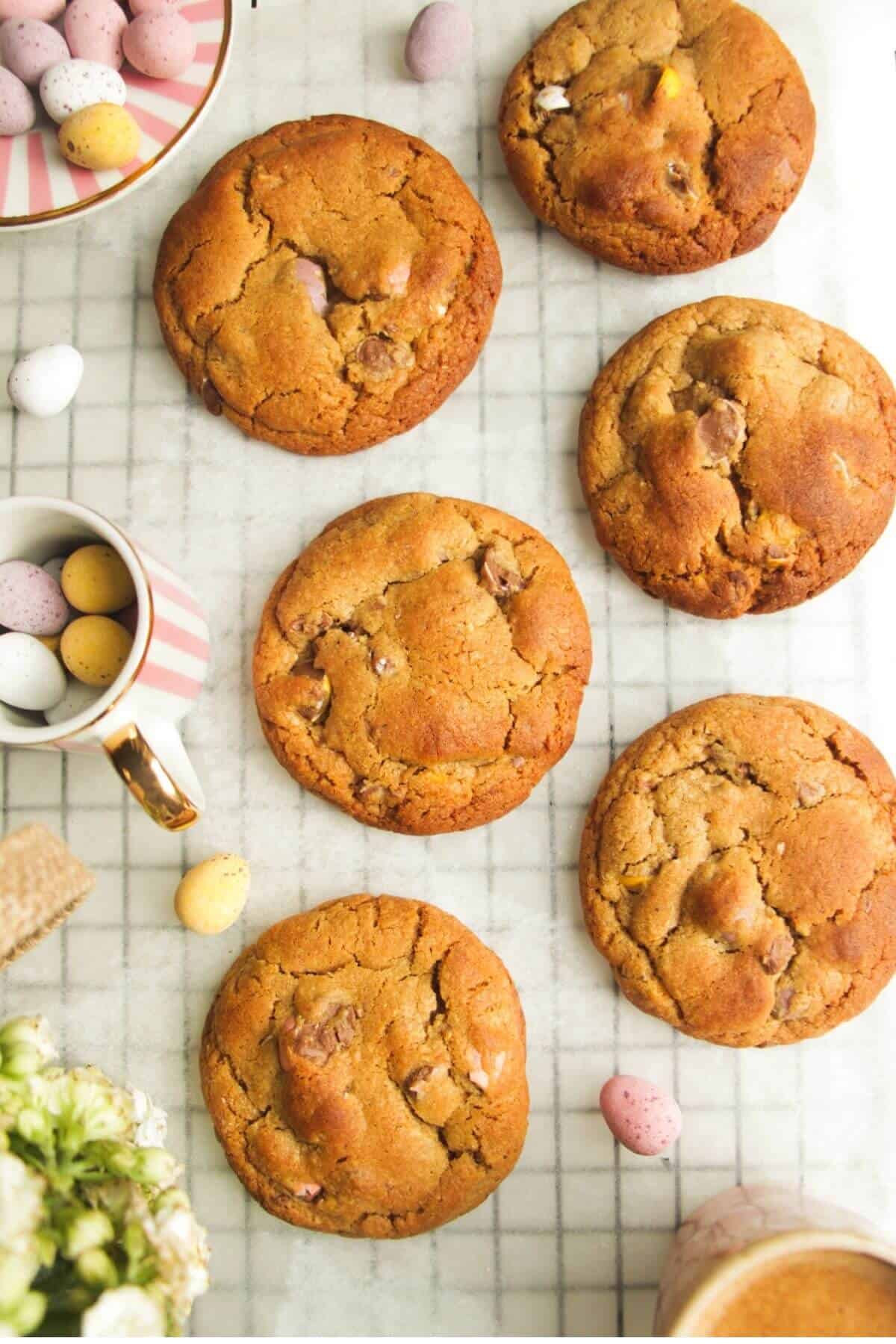 Mini egg cookies on baking paper, with more mini eggs on the side.