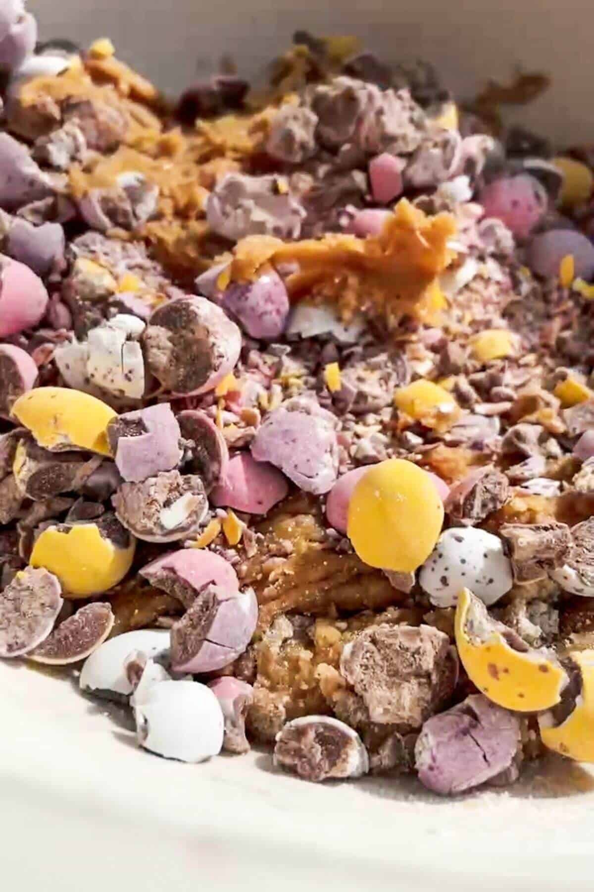 Crushed mini eggs added to cookie dough mixture in a large mixing bowl.