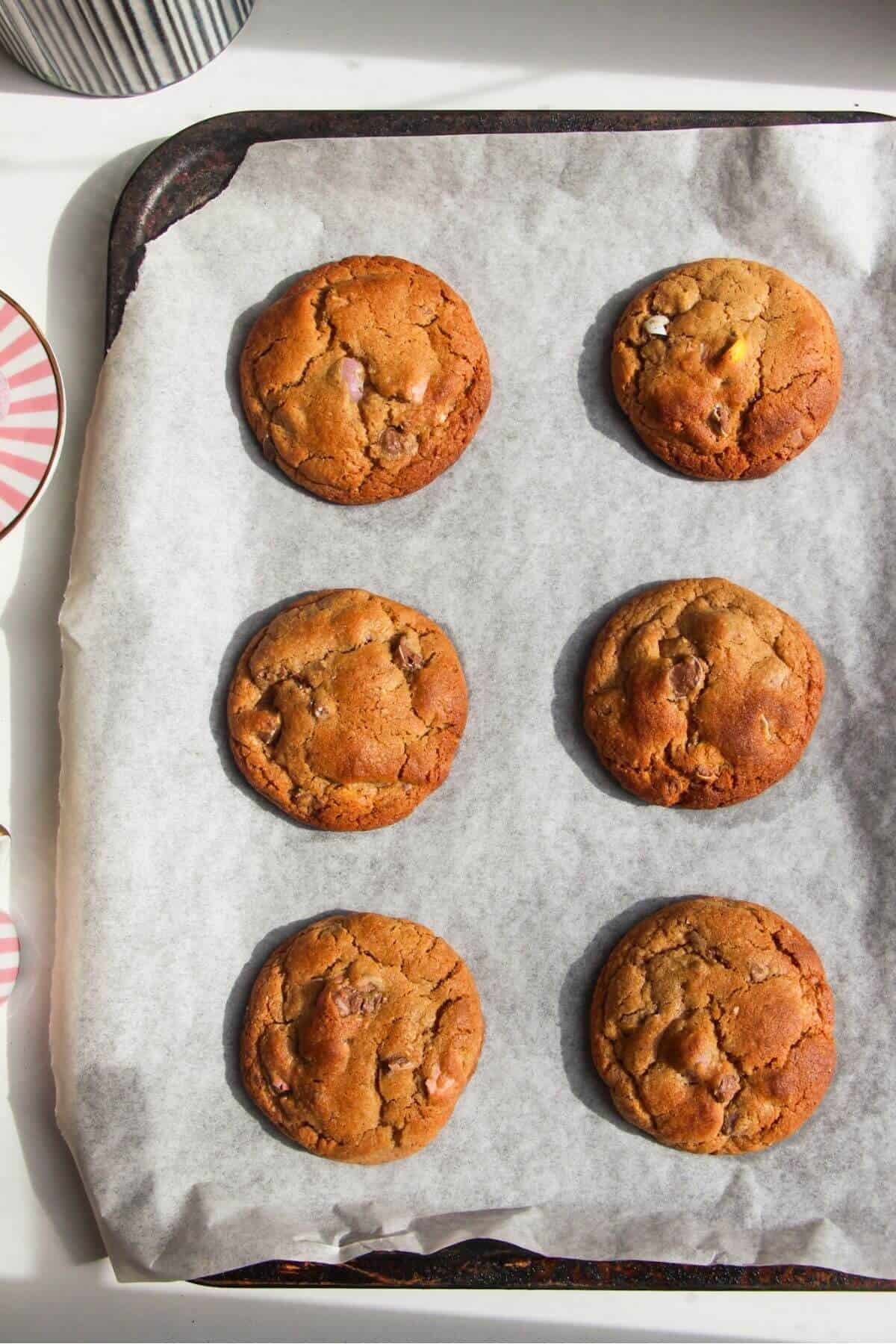 Six baked mini egg cookies on a baking paper lined baking tray.