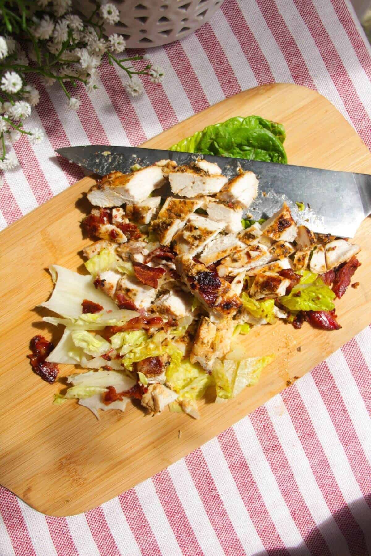 Chicken, bacon and lettuce on a wooden board, chopped with a knife.