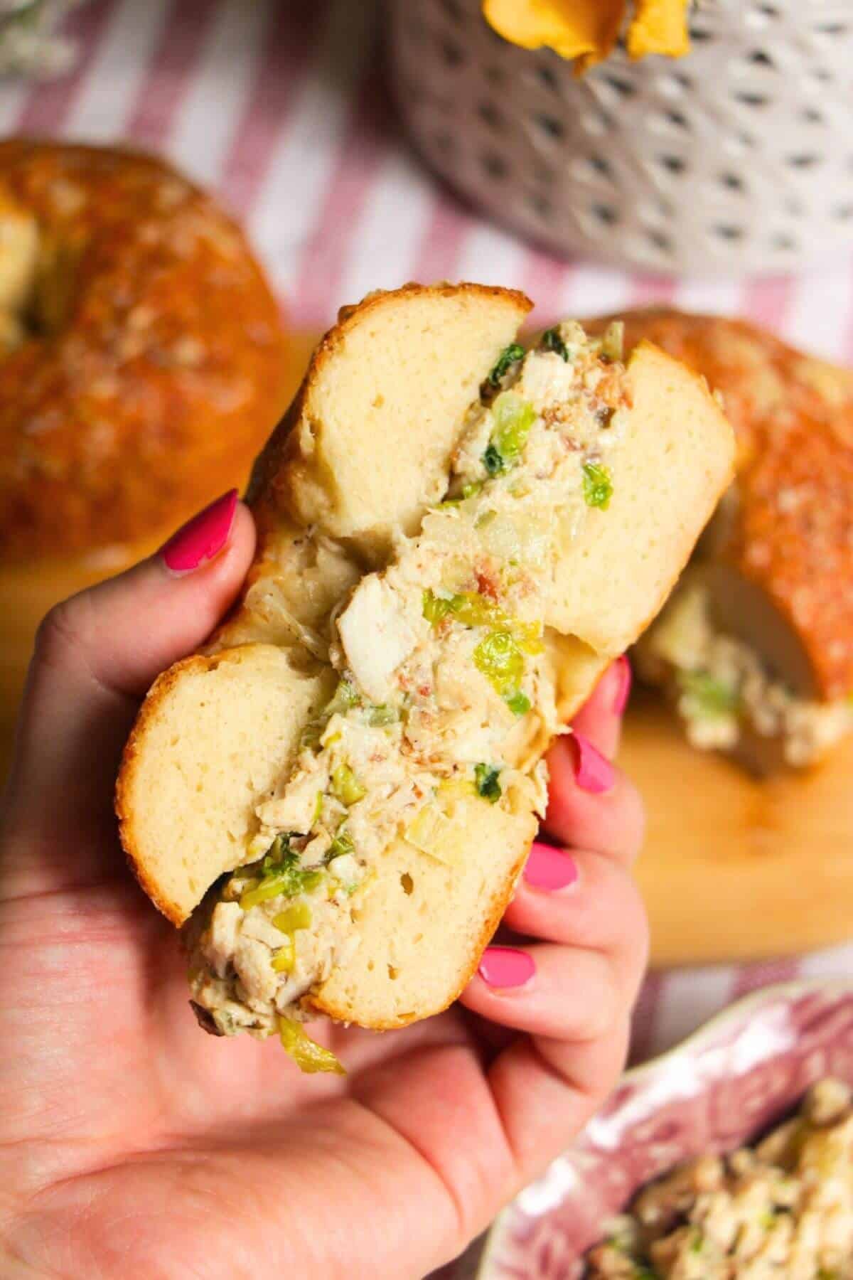 Hand holding half a bagel filled with chicken Caesar salad.
