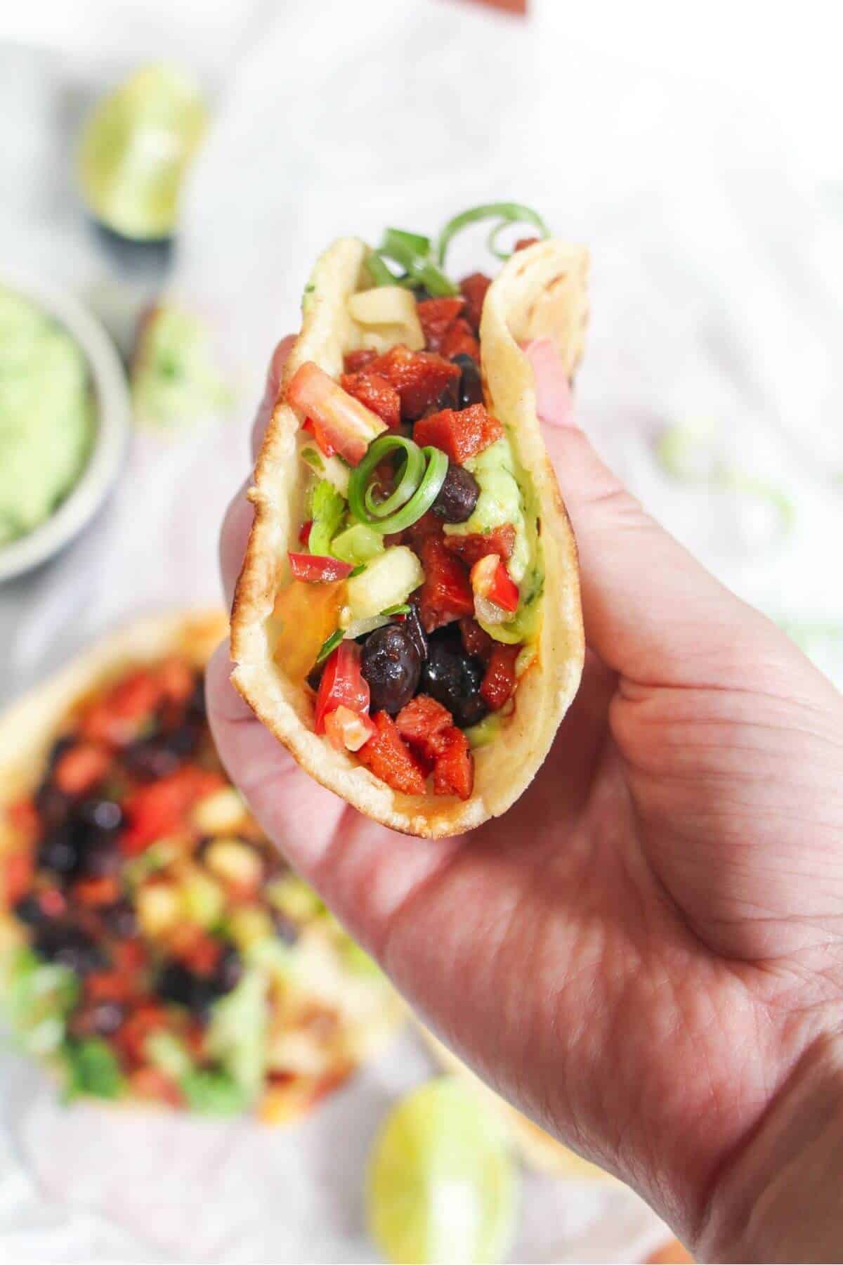 Hand holding up a chorizo and black bean taco with more tacos in the background.