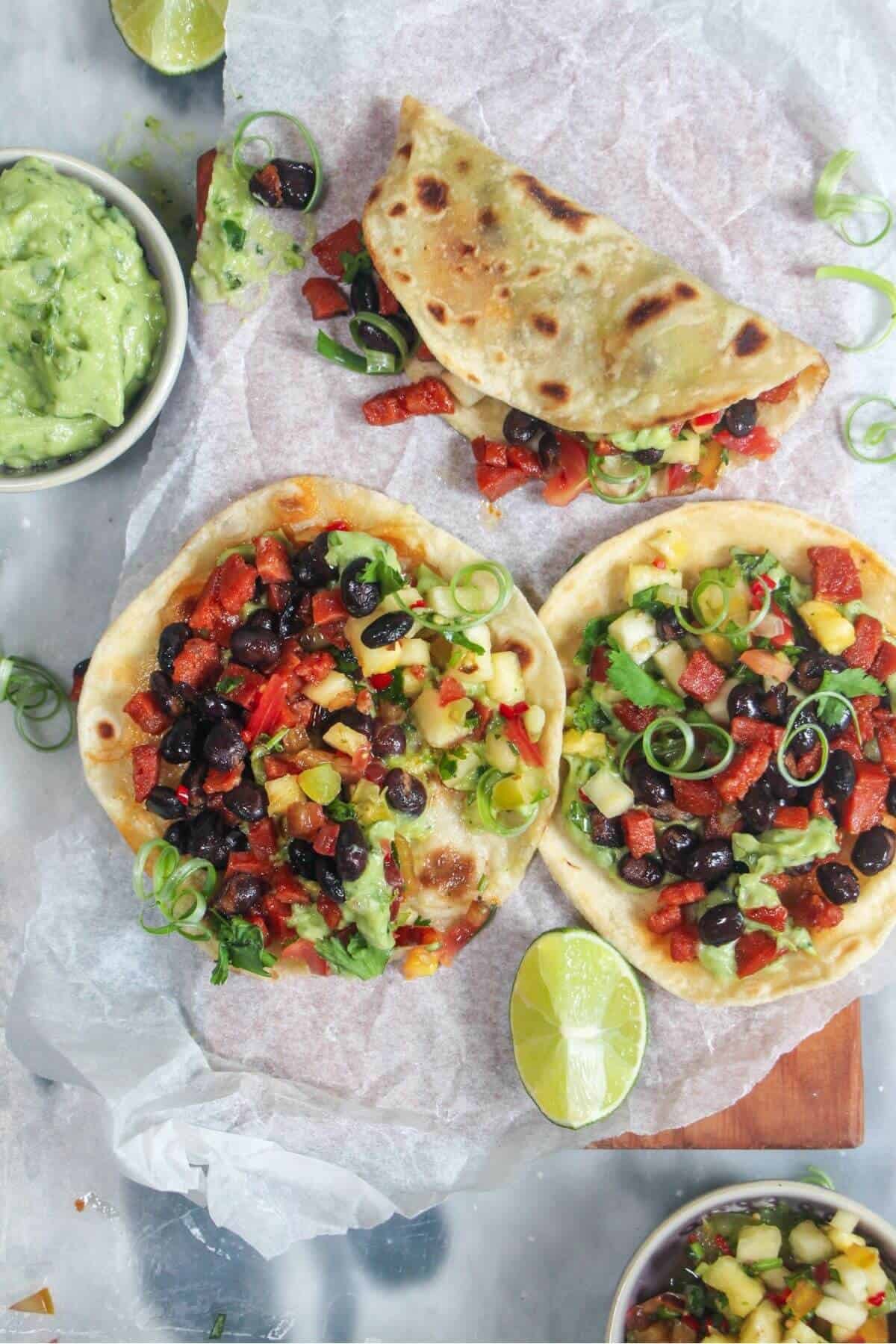 3 chorizo black bean tacos on a baking paper lined board, with whipped avocado and salsa on the side.