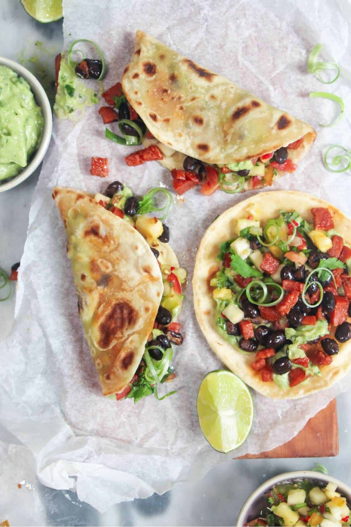3 chorizo black bean tacos on a baking paper lined board, with whipped avocado and salsa on the side.