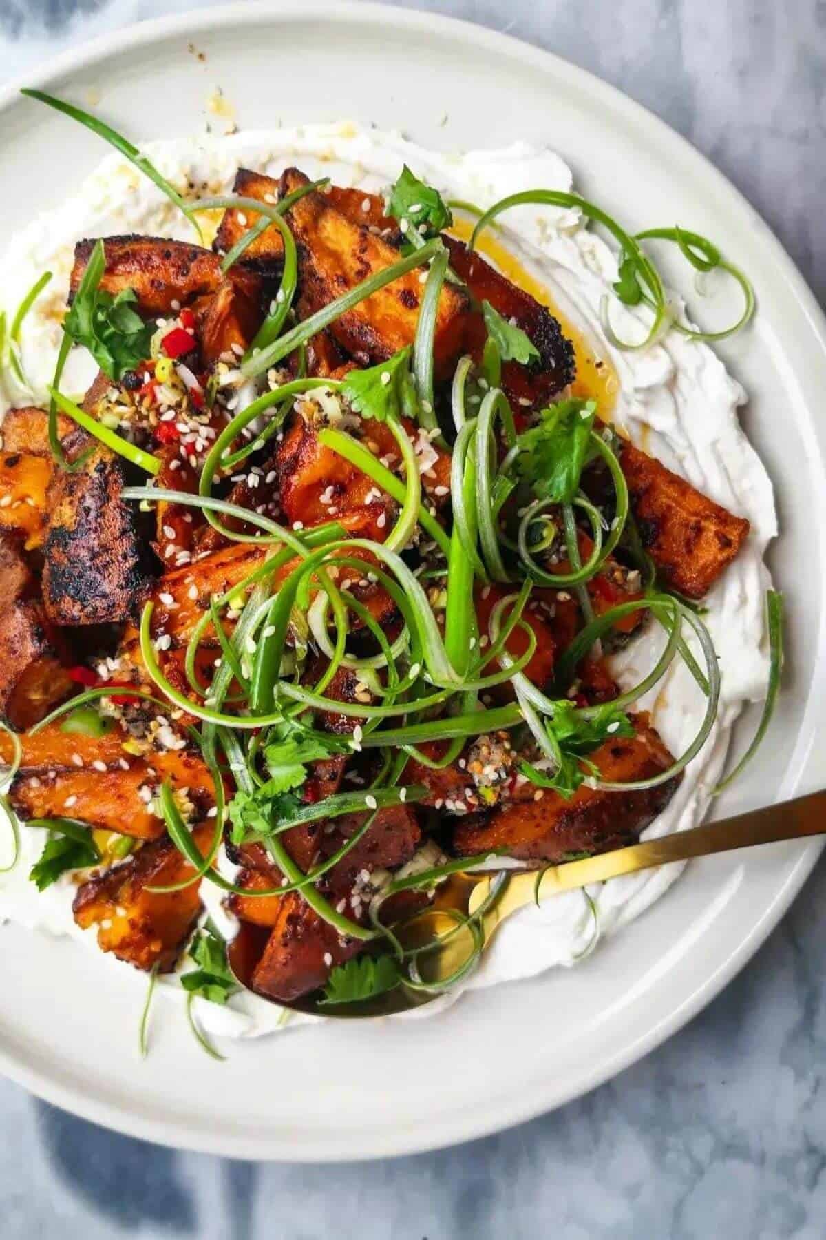 Miso roasted sweet potatoes on labneh, with chilli lime salsa on top on a white plate.