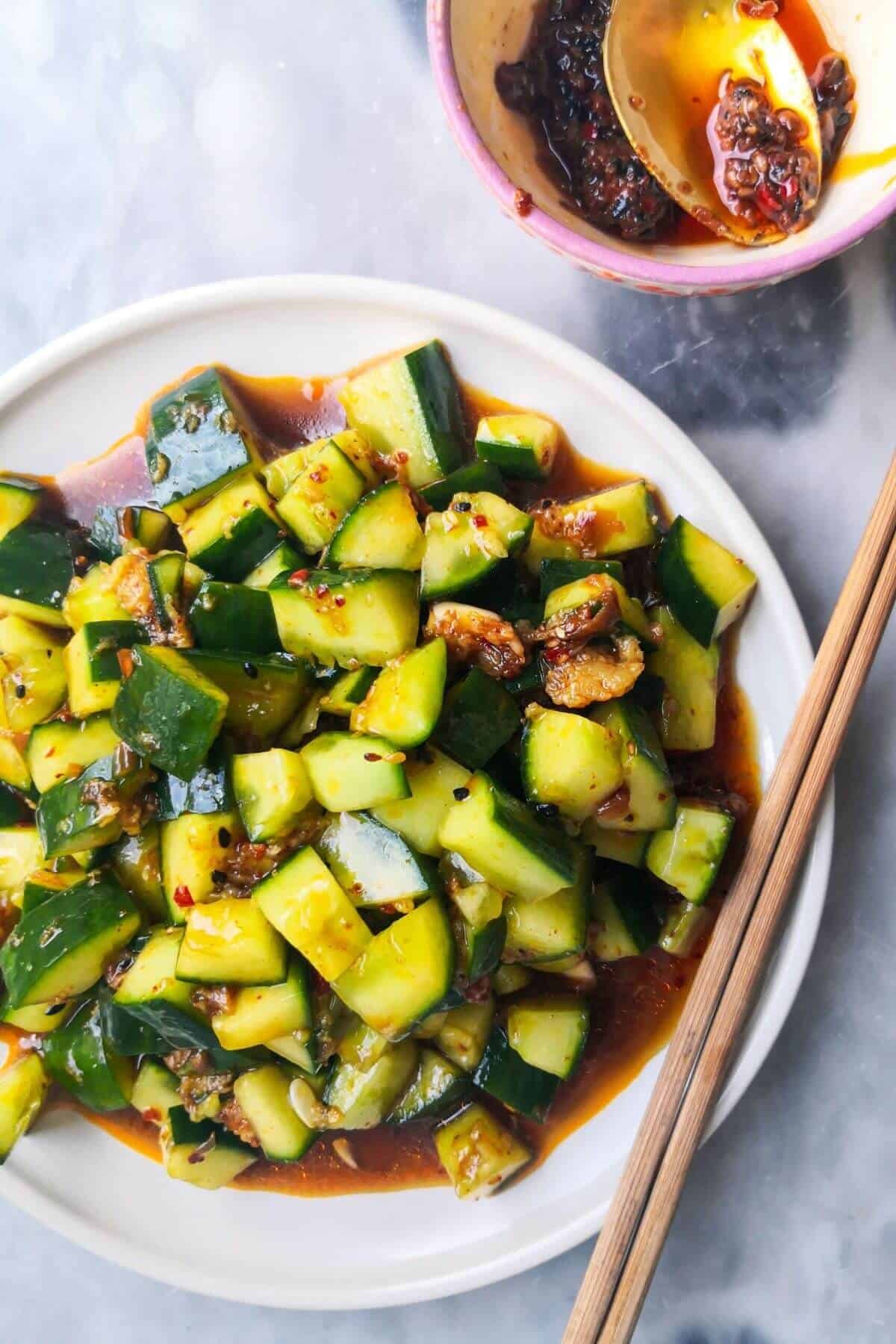 Smacked cucumber salad on a white plate with chopsticks on the side, with a small bowl of chilli oil.