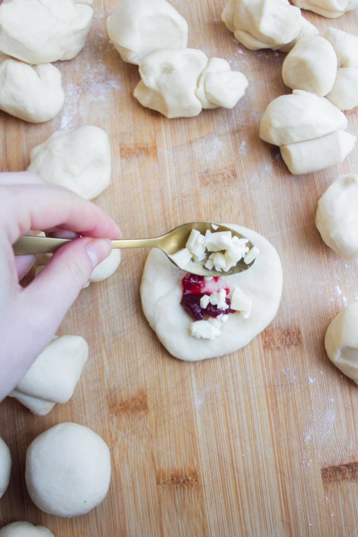 Hand holding a small spoon adding cheese to the middle of a piece of dough.