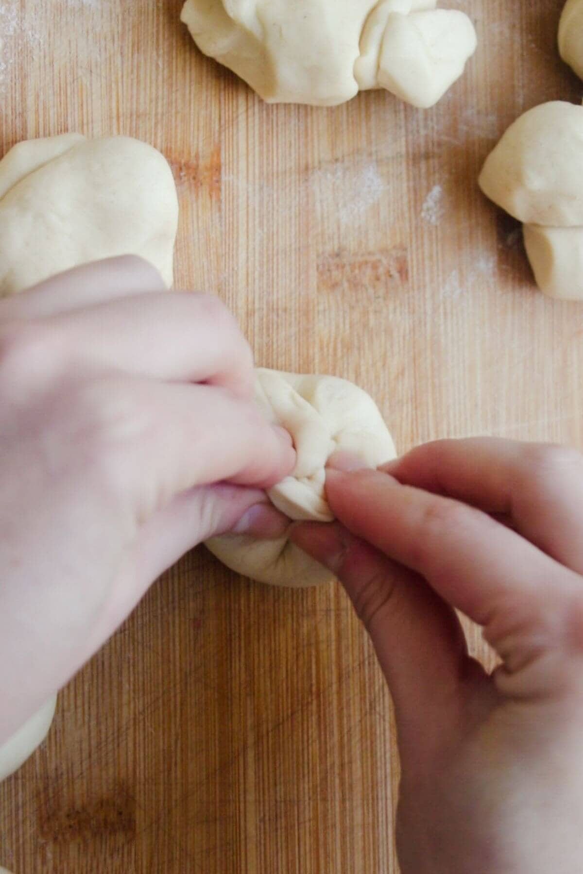 2 hands pinching dough ball together on a wooden board.
