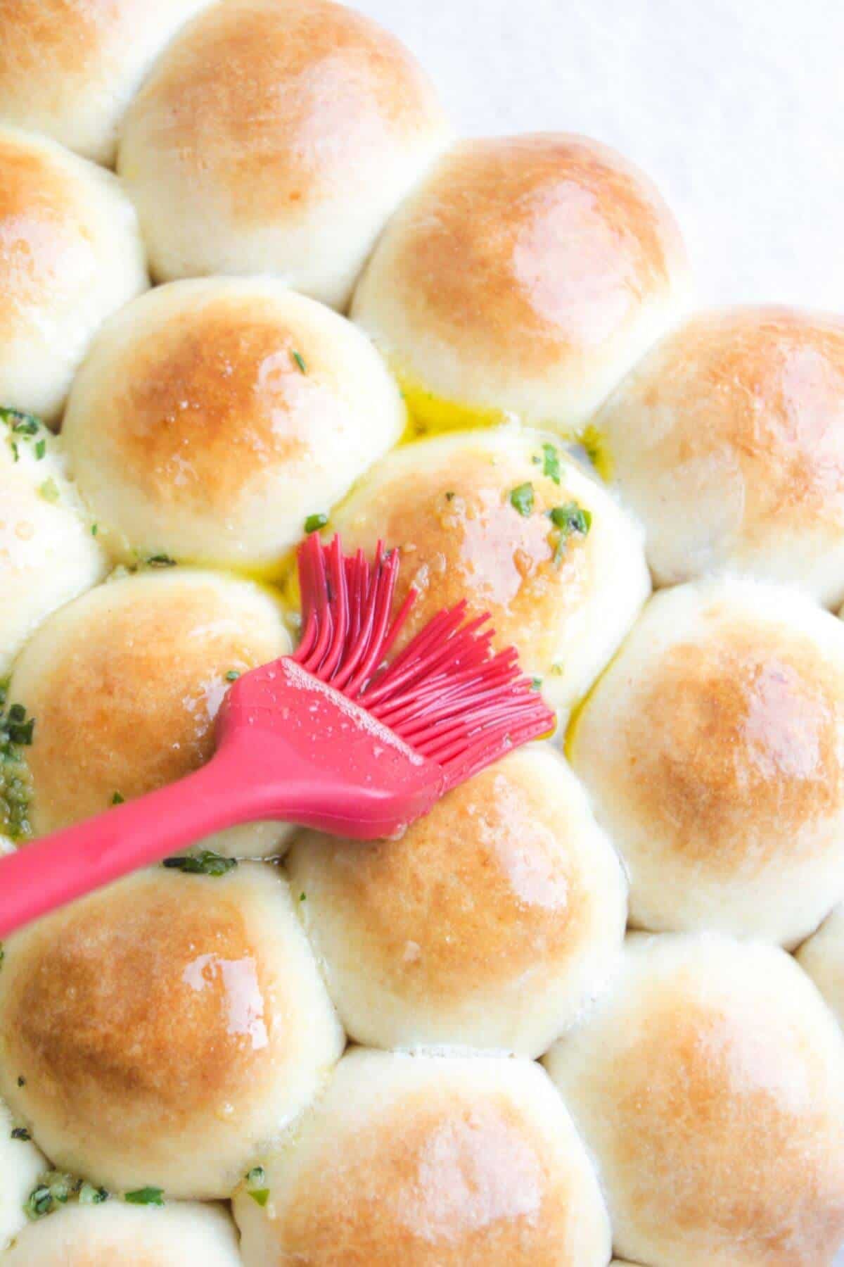 Close up of a red brush brushin golden dough balls with garlic butter.