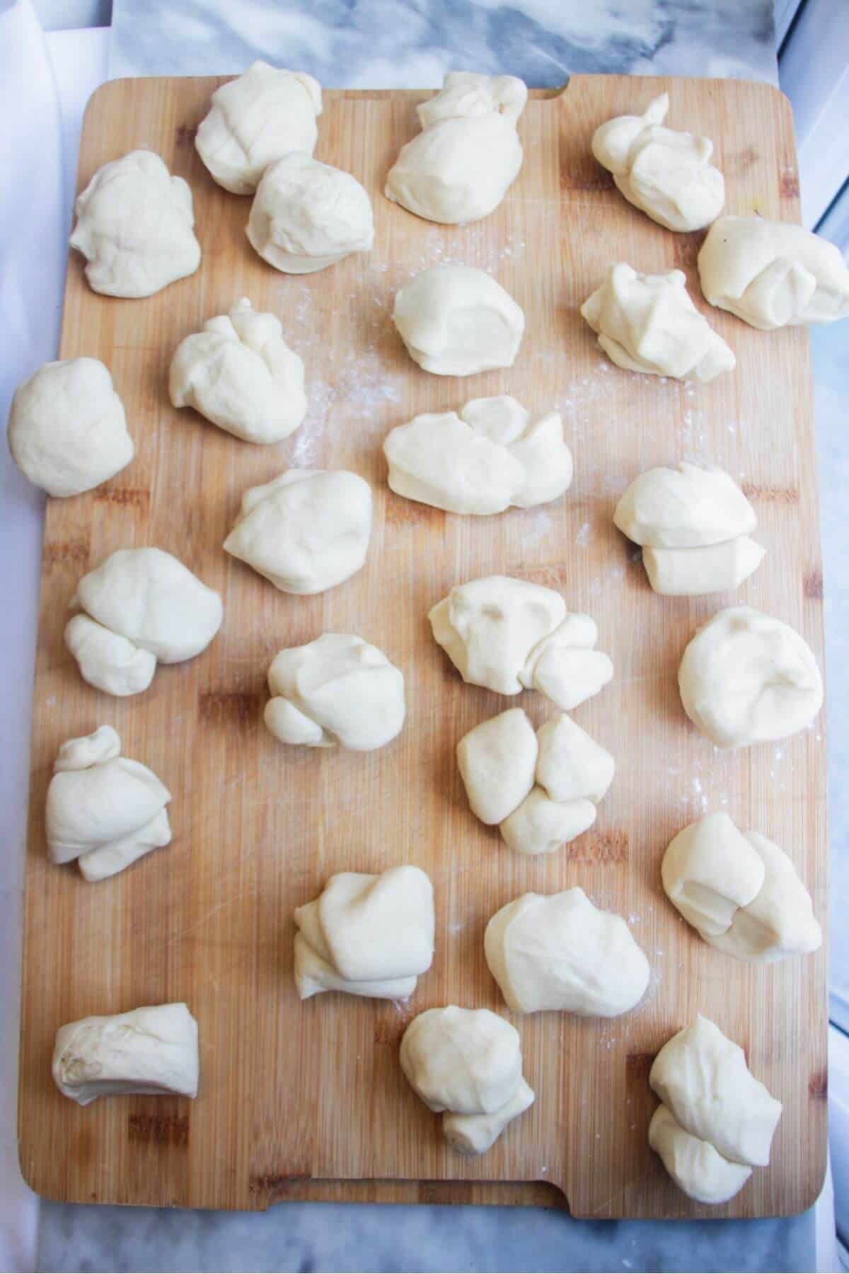 Wooden board with lots of pieces of dough on it.