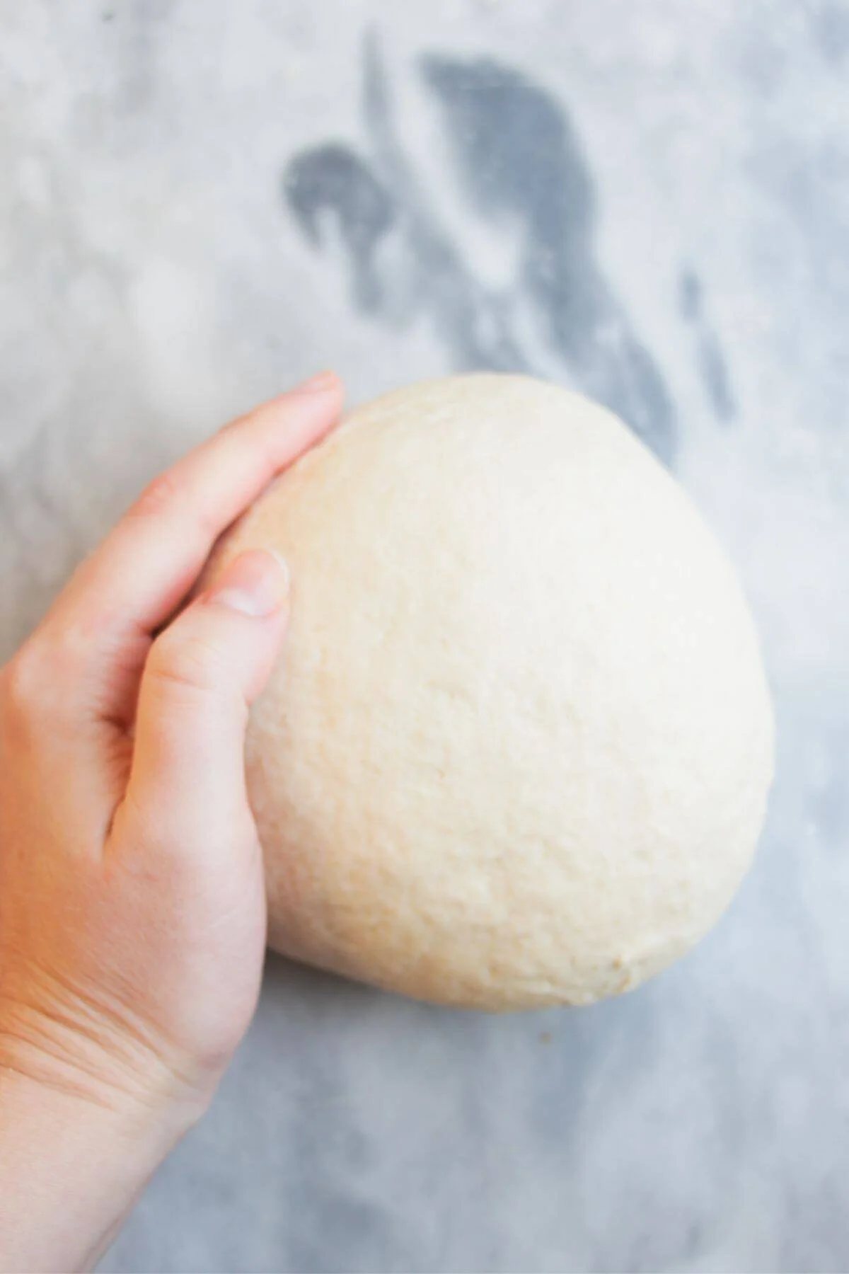 Hand holding kneaded dough on a grey marble background.