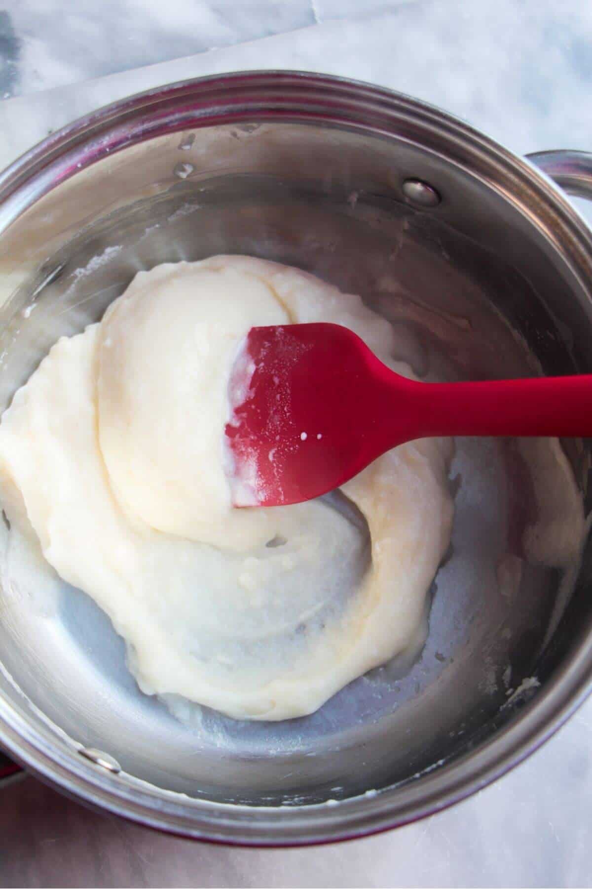 Small red spatula stirring the tangzhong paste in a small silver pot.