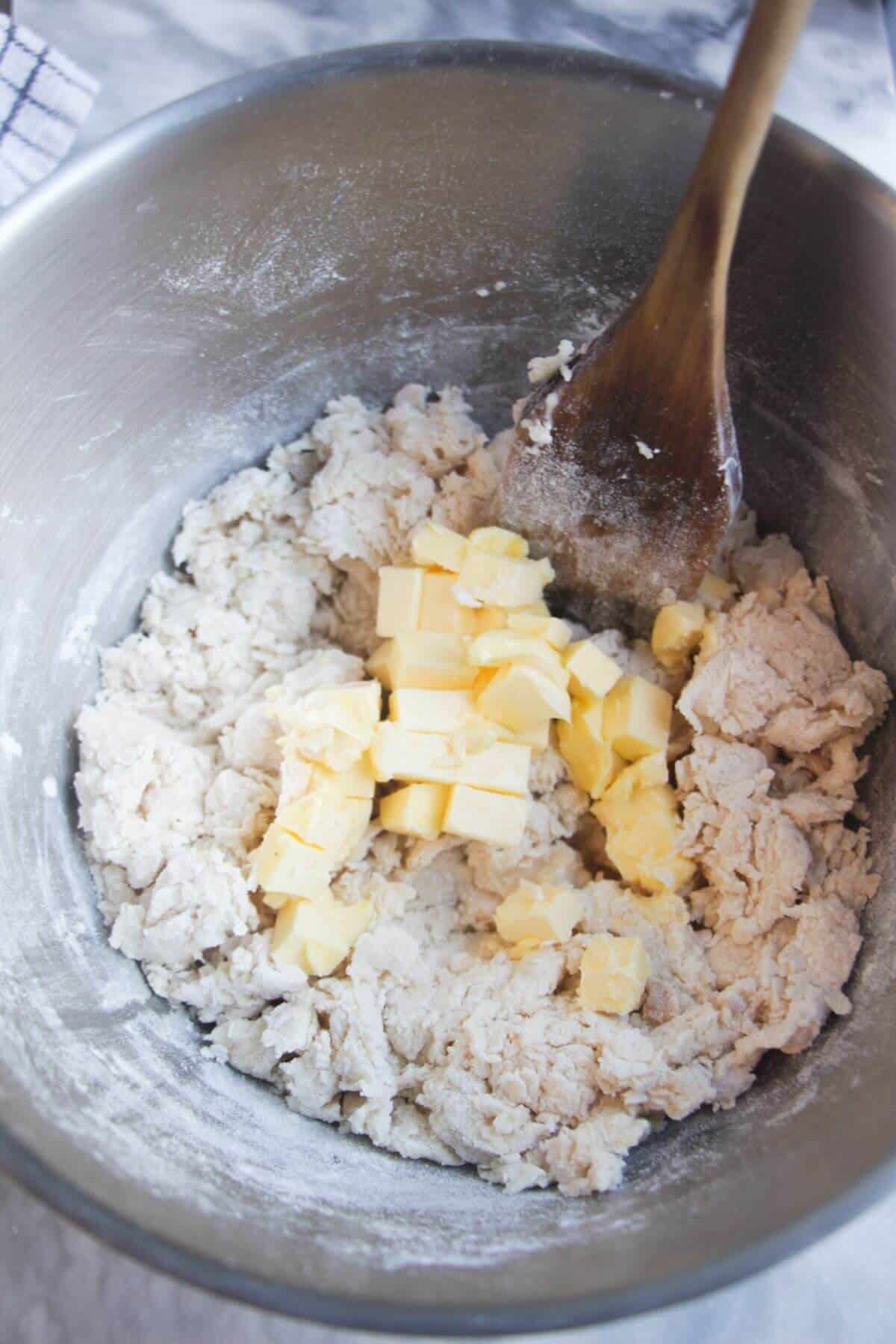 Cubes of butter being added to a mixing bowl with dough in it.