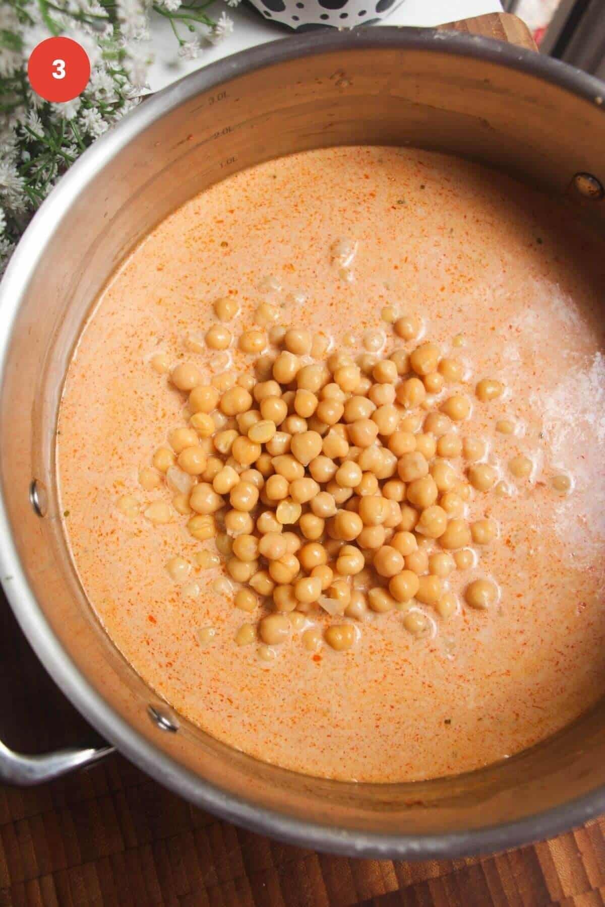 Chickpeas added to red curry coconut sauce in a pan.