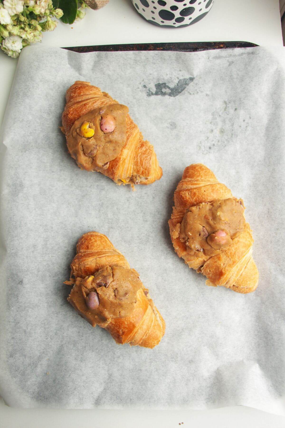Three unbaked cookie dough stuffed croissants on a lined baking tray.